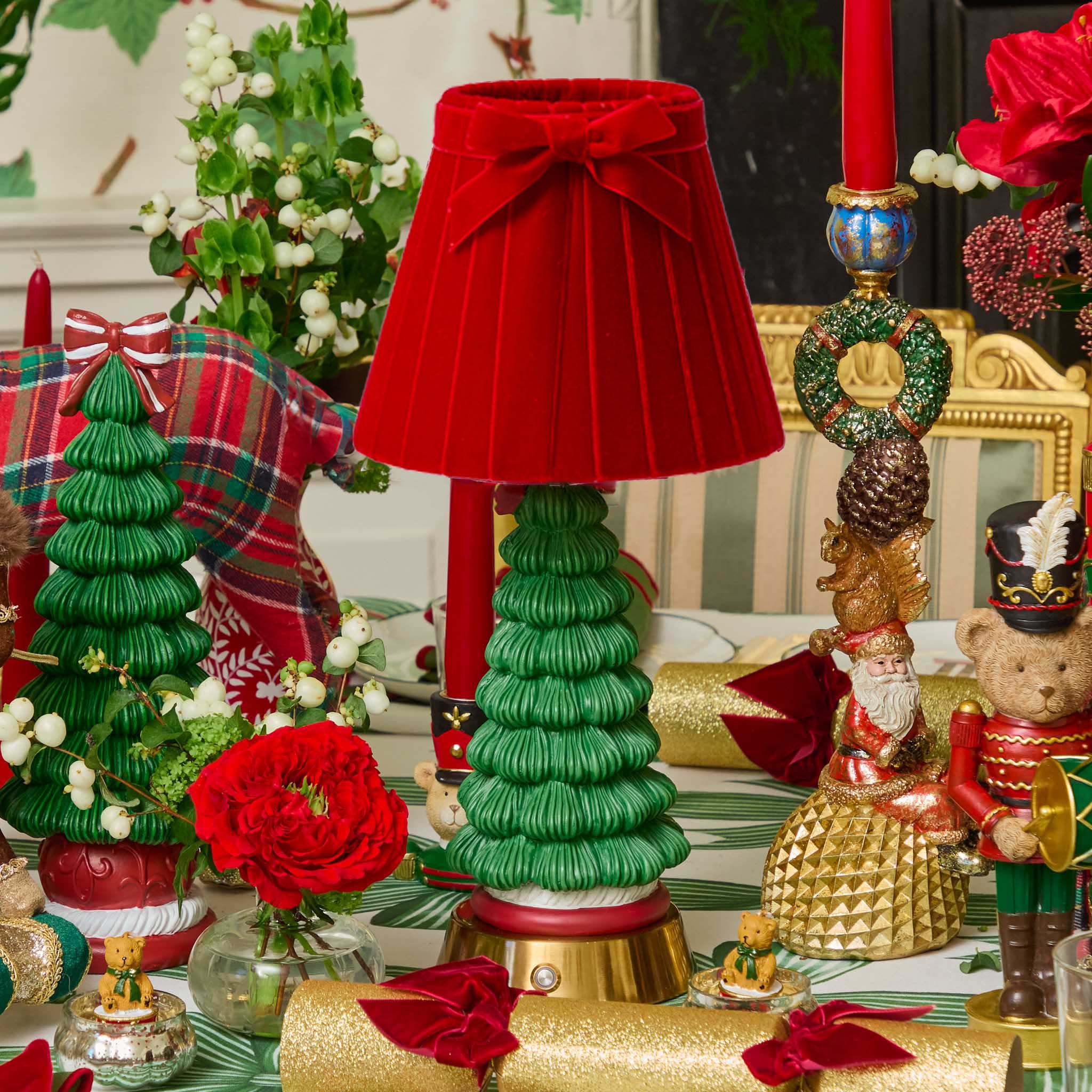 Decorative Christmas table setting with a red lamp, green tree-shaped candle holder, and festive decorations.