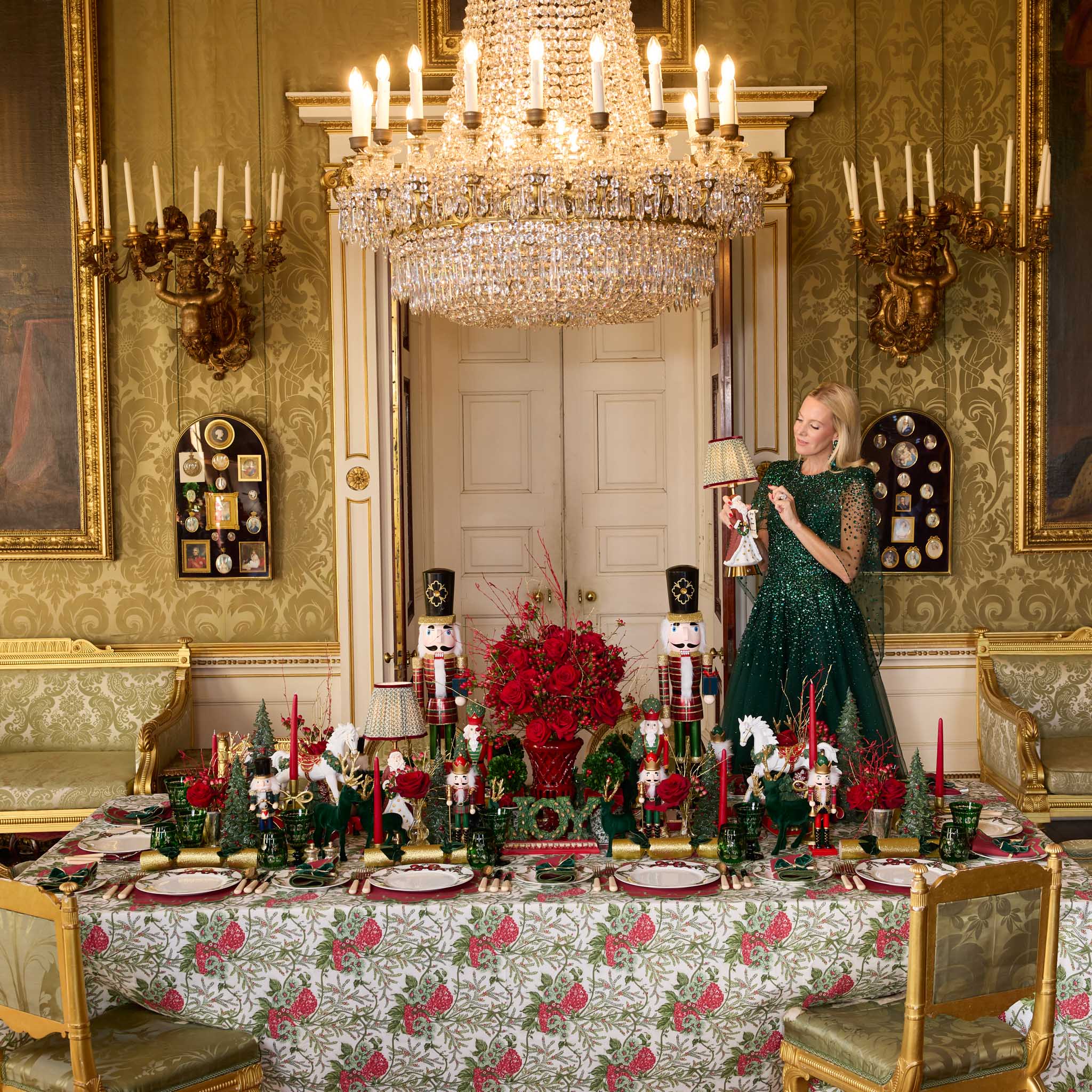 Elegant dining room with a woman in a green dress standing by a table set for Christmas.