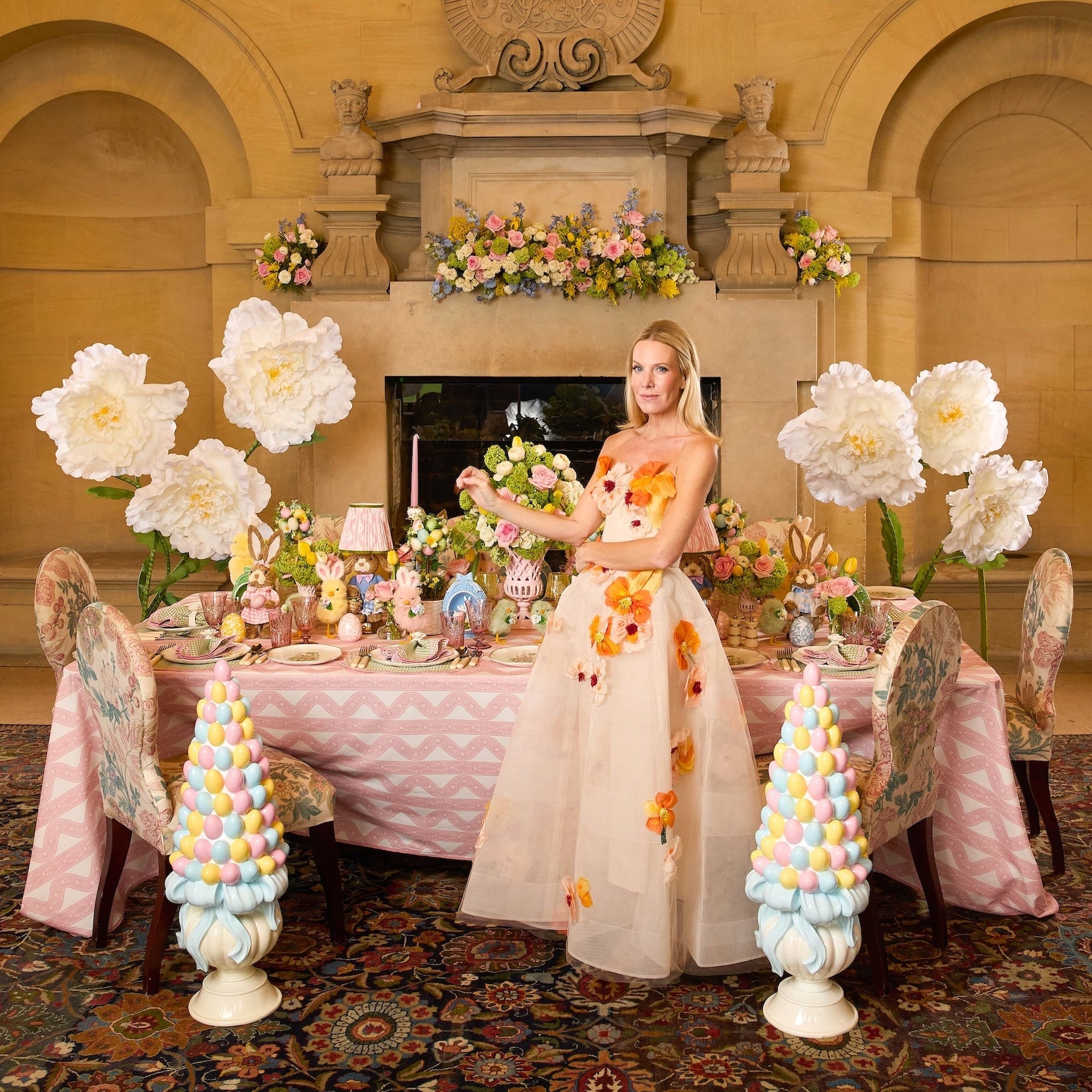 Woman in a floral dress standing in a decorated room with flowers and table settings.