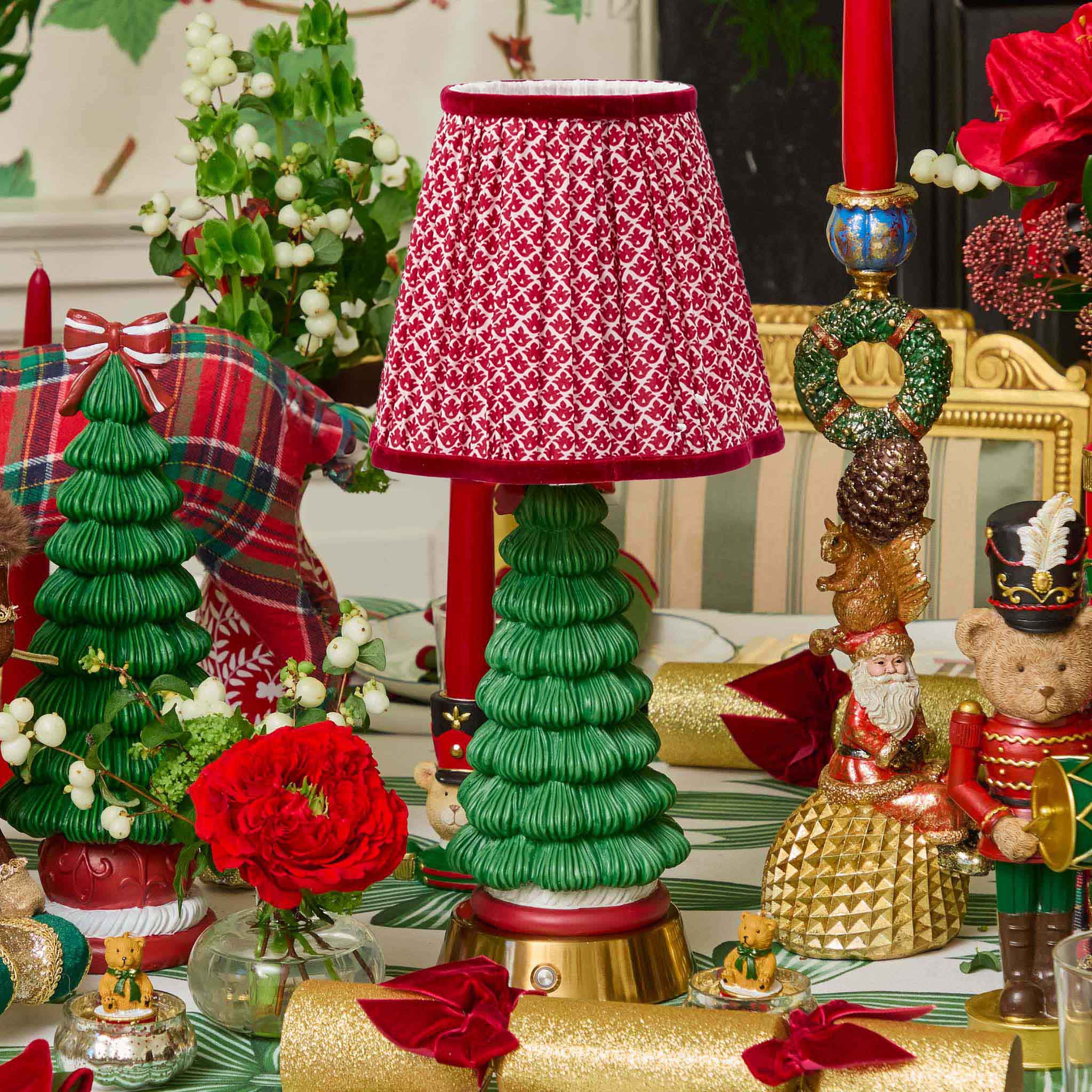 Decorative Christmas table setting with a red and white lampshade, green tree-shaped candle holder, and festive decorations.
