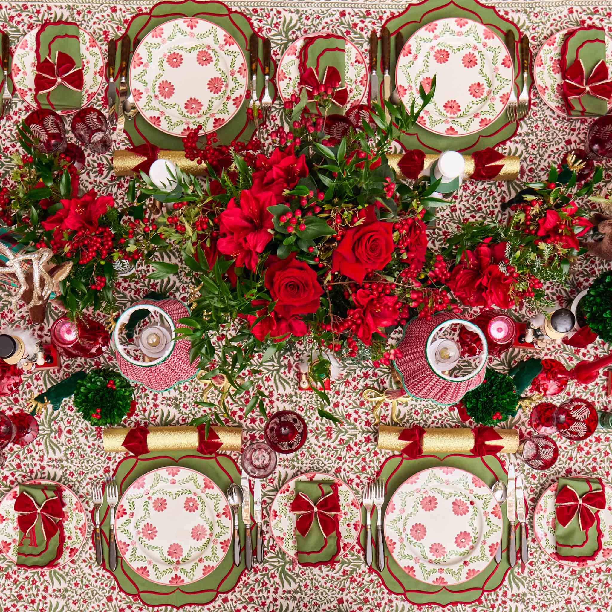 Decorative Christmas table setting with red and green floral patterns on plates and tablecloth.