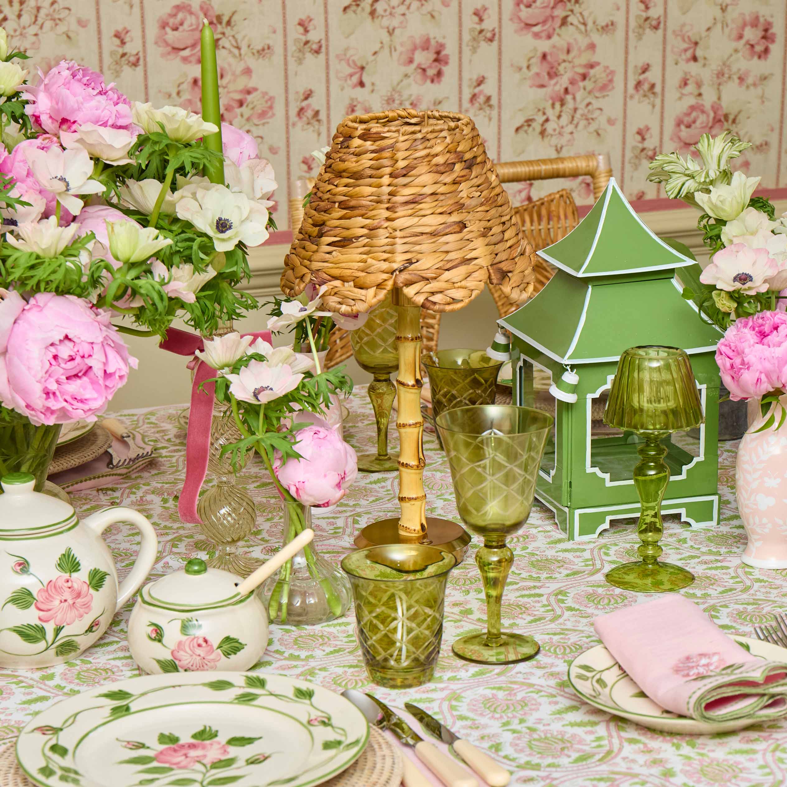 Decorative table setting with floral teaware, green glassware, and a small pagoda model.