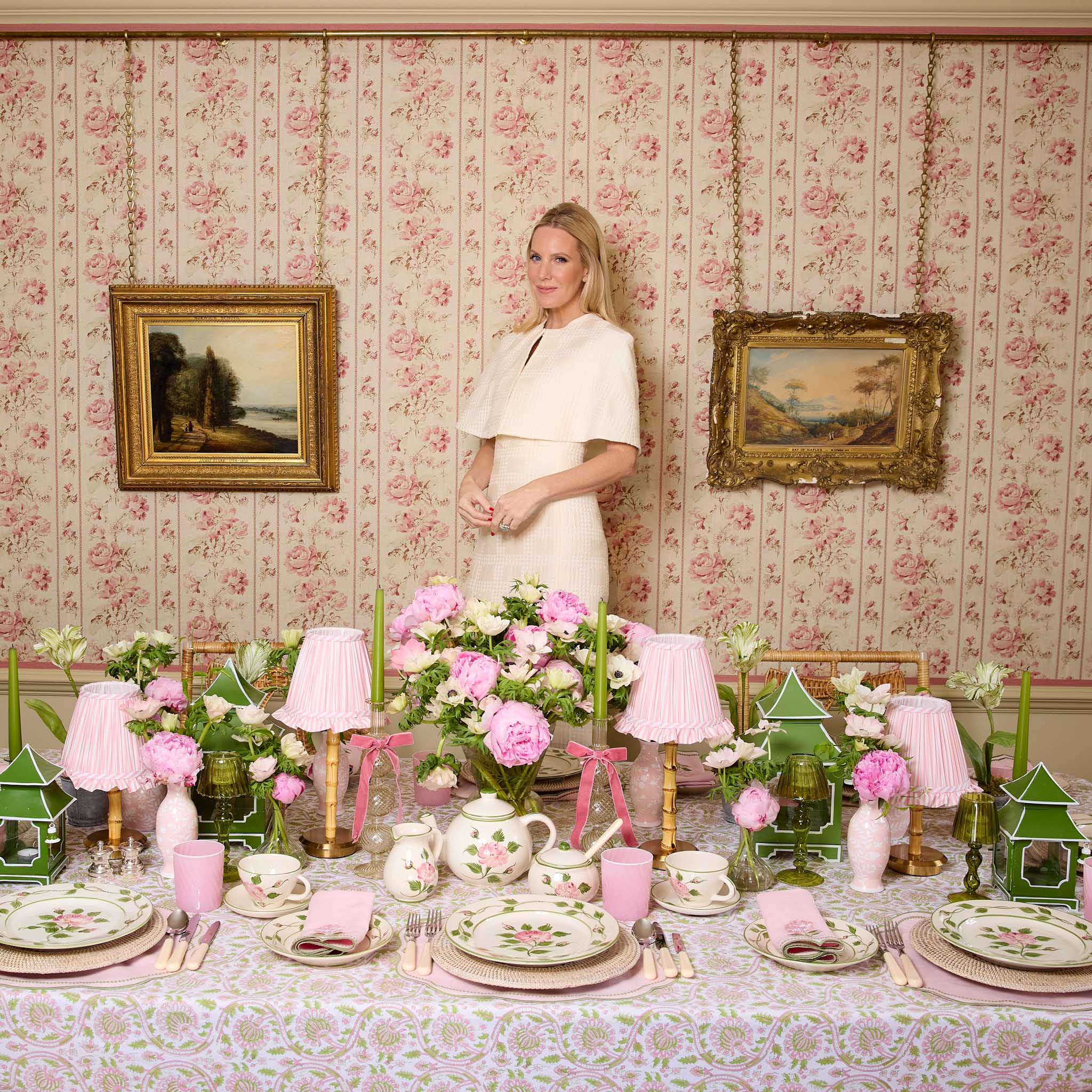 Woman standing in a room with floral wallpaper and a table set for a formal dinner.