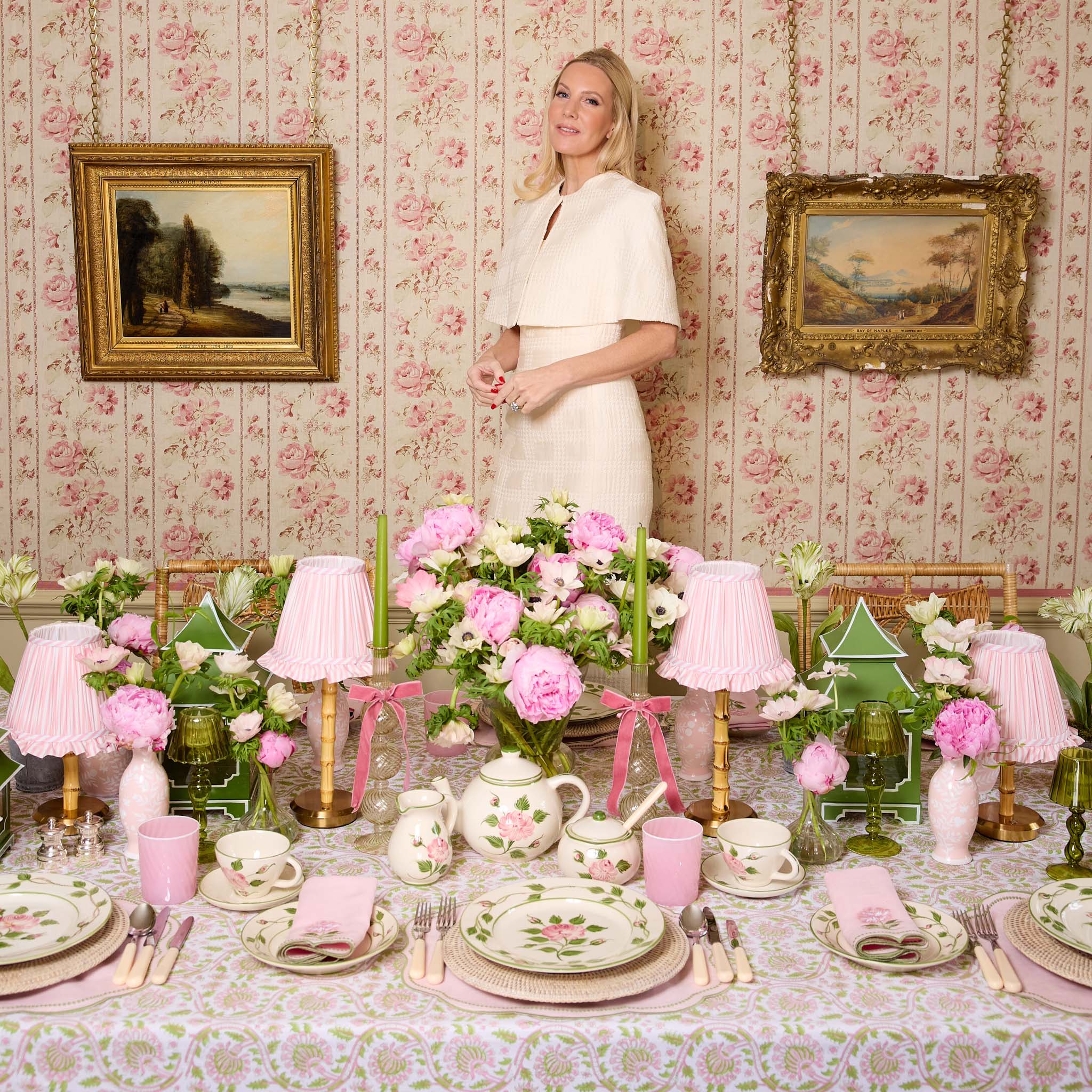Woman standing in a room with floral wallpaper and a table set for a tea party.
