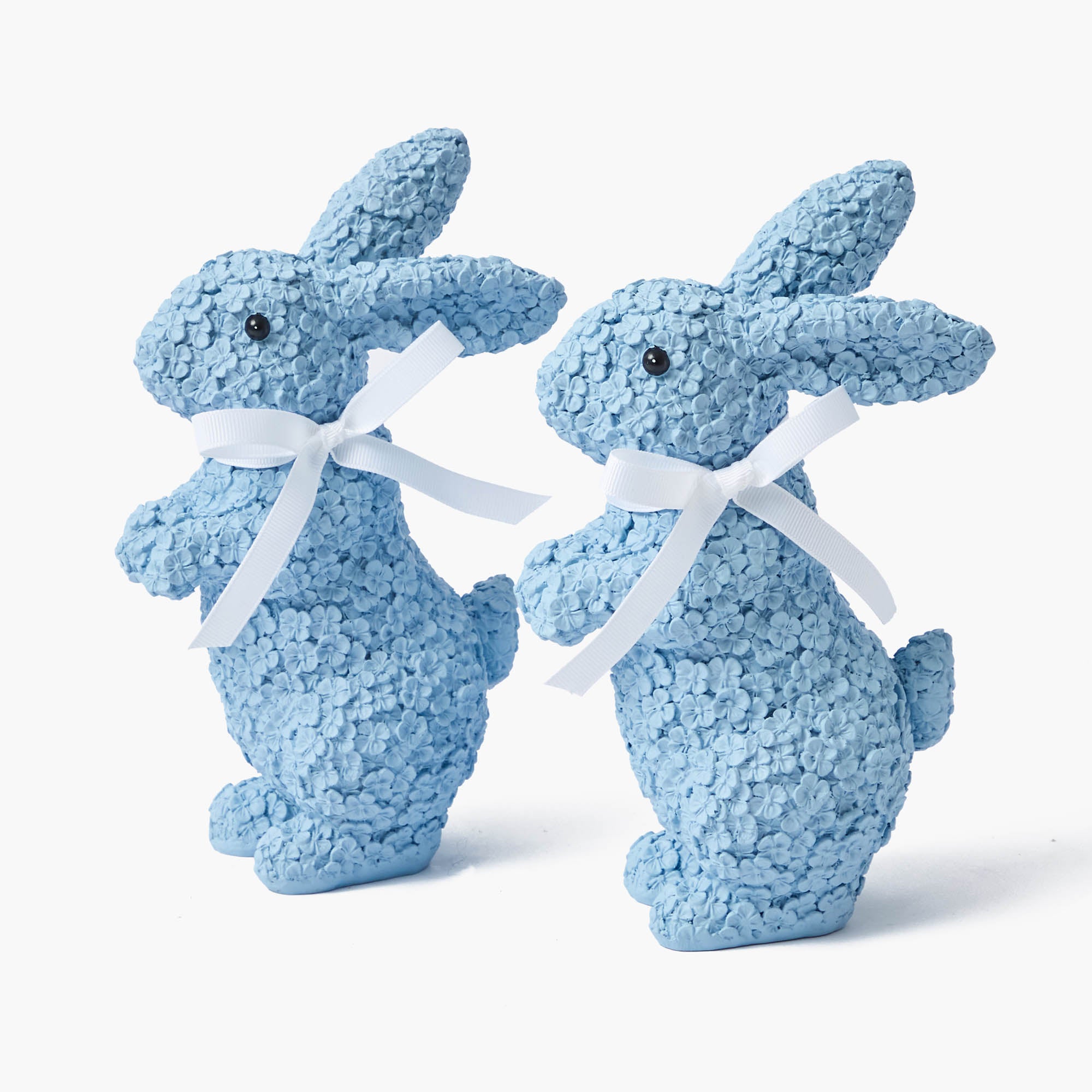 Two blue floral patterned resin bunnies with white bows around their necks.