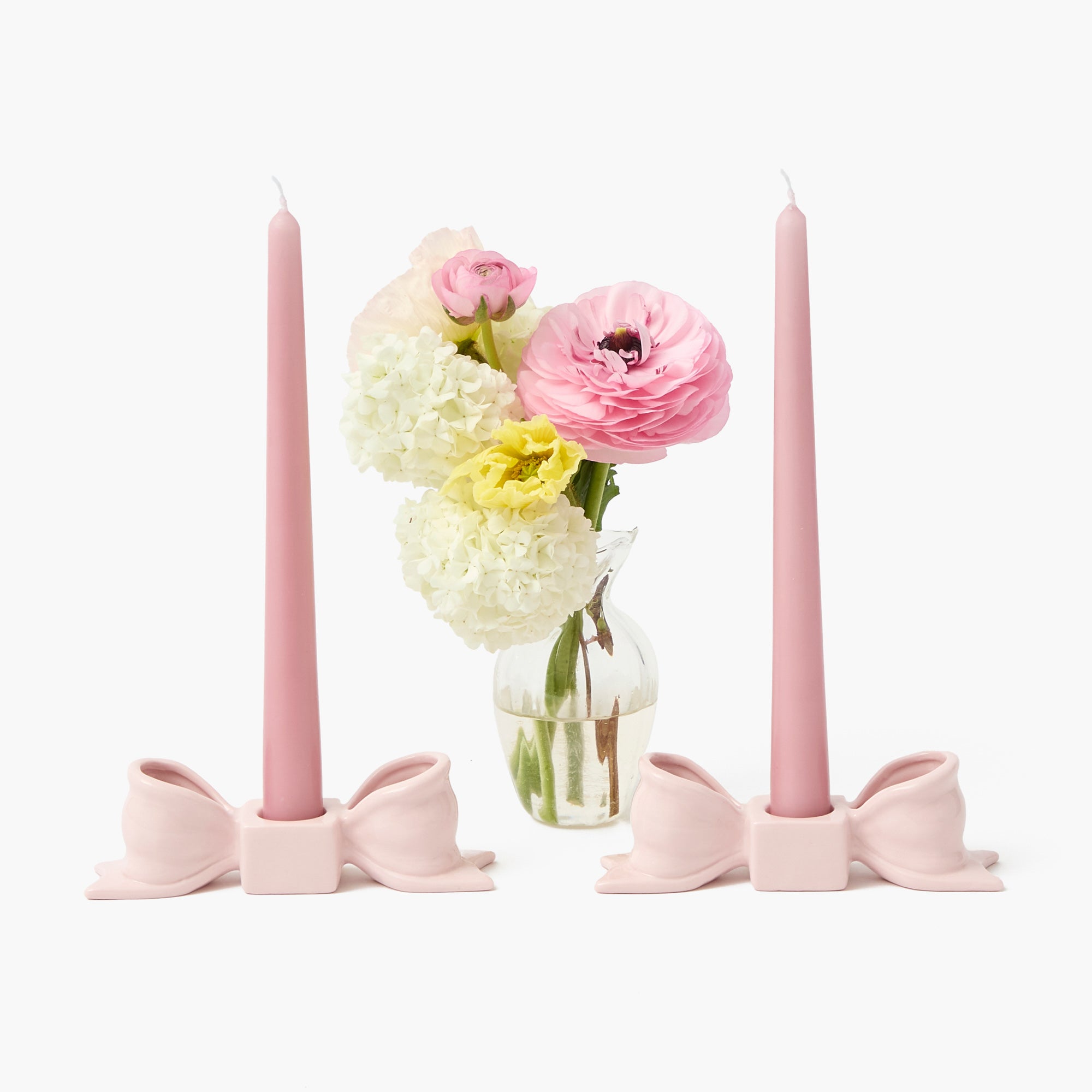 Pink candles with bow holders and a vase of flowers on a white background