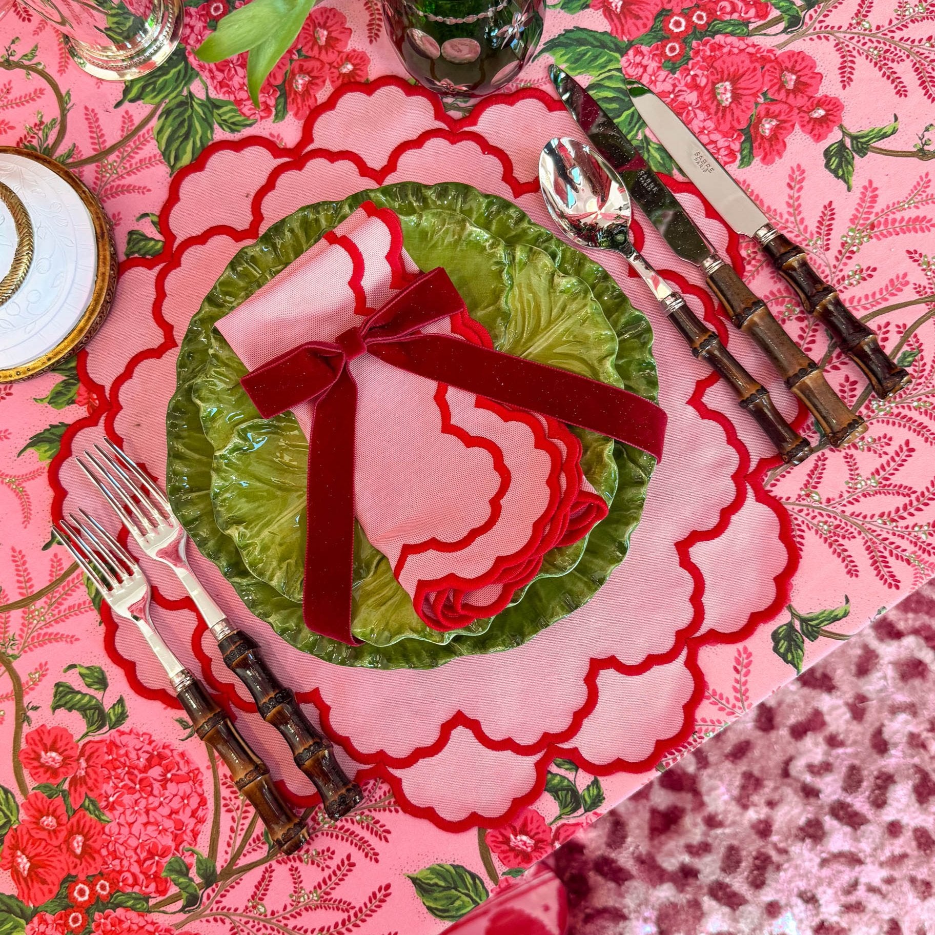 A set of pink placemats and napkins with a floral pattern, displayed with a green plate and red bow.