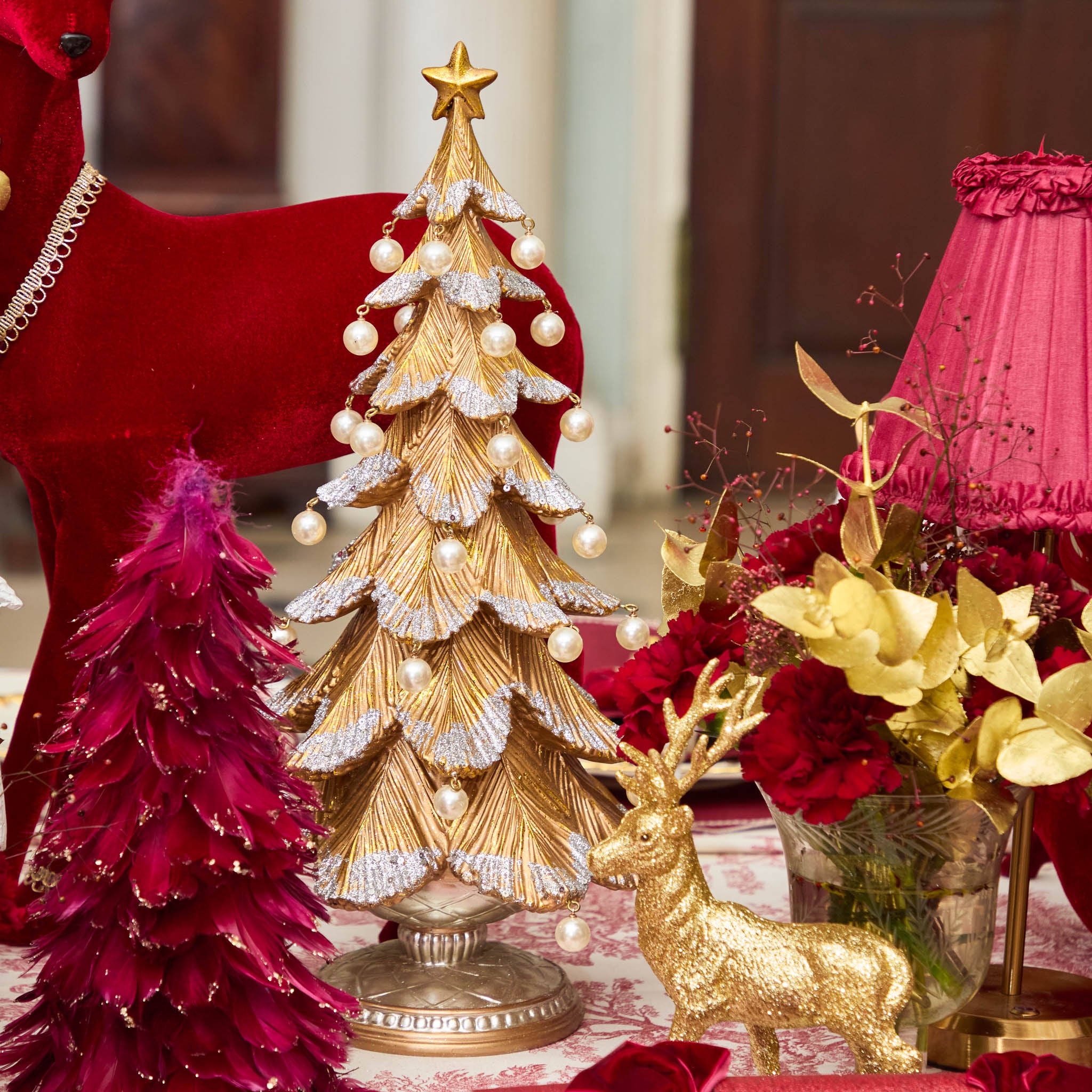 Decorative Christmas scene with gold tree, red and gold reindeer, and flowers on a table.