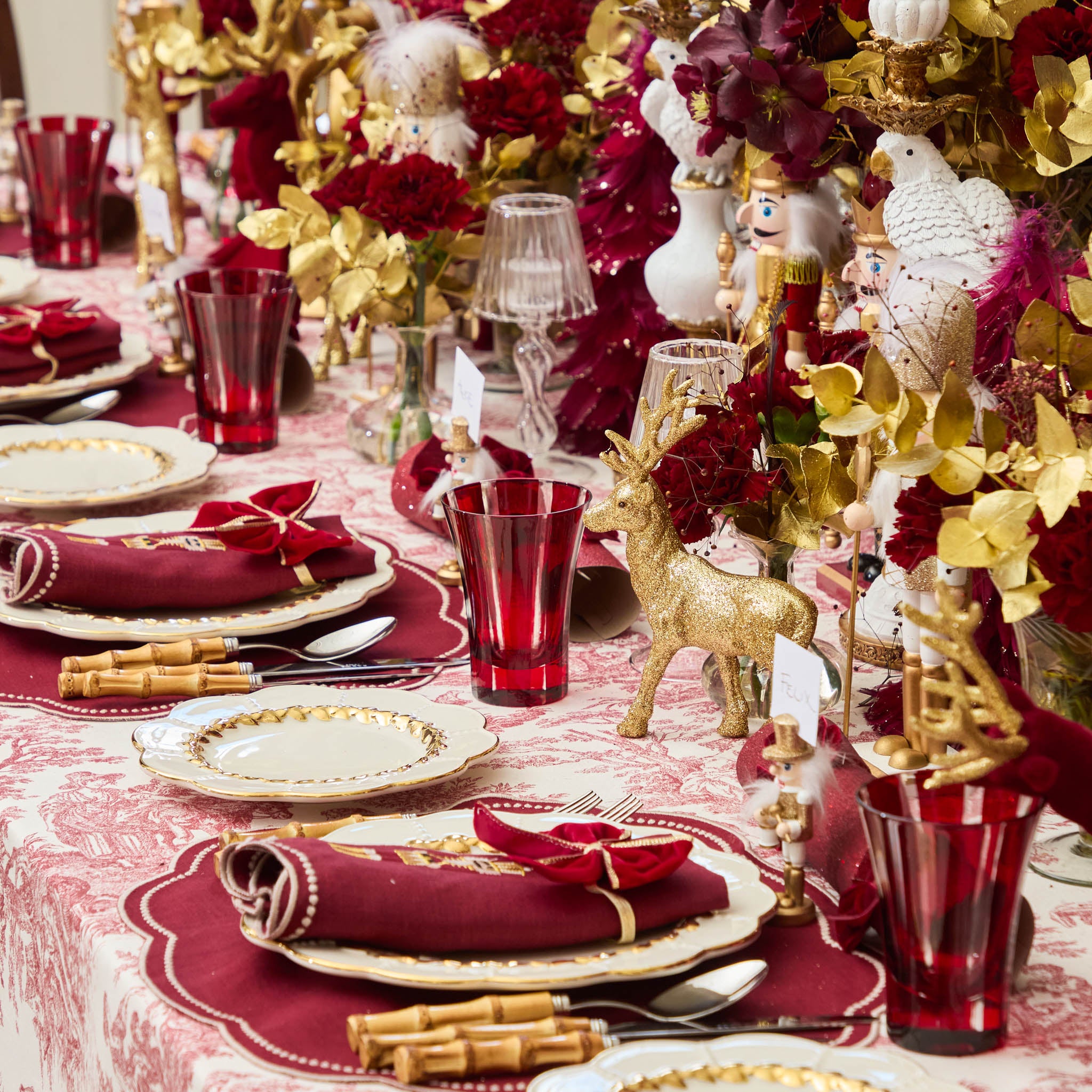 Decorative Christmas table setting with red and gold tableware, ornaments, and floral arrangements.