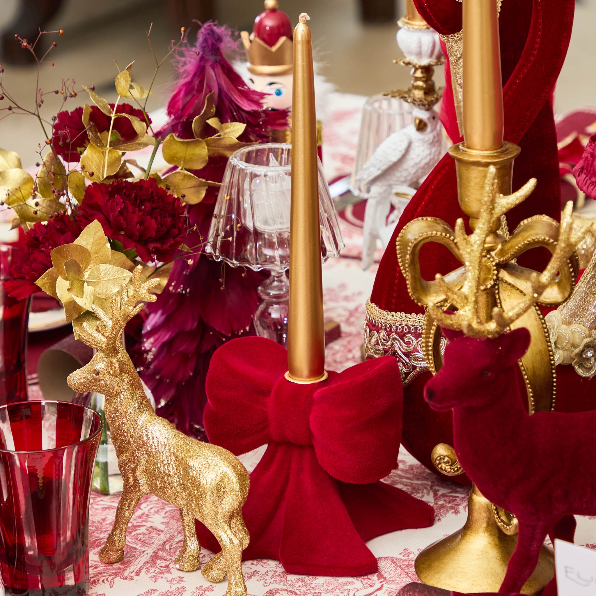 Decorative table setting with gold deer figurines, red bows, and candles on a festive background.