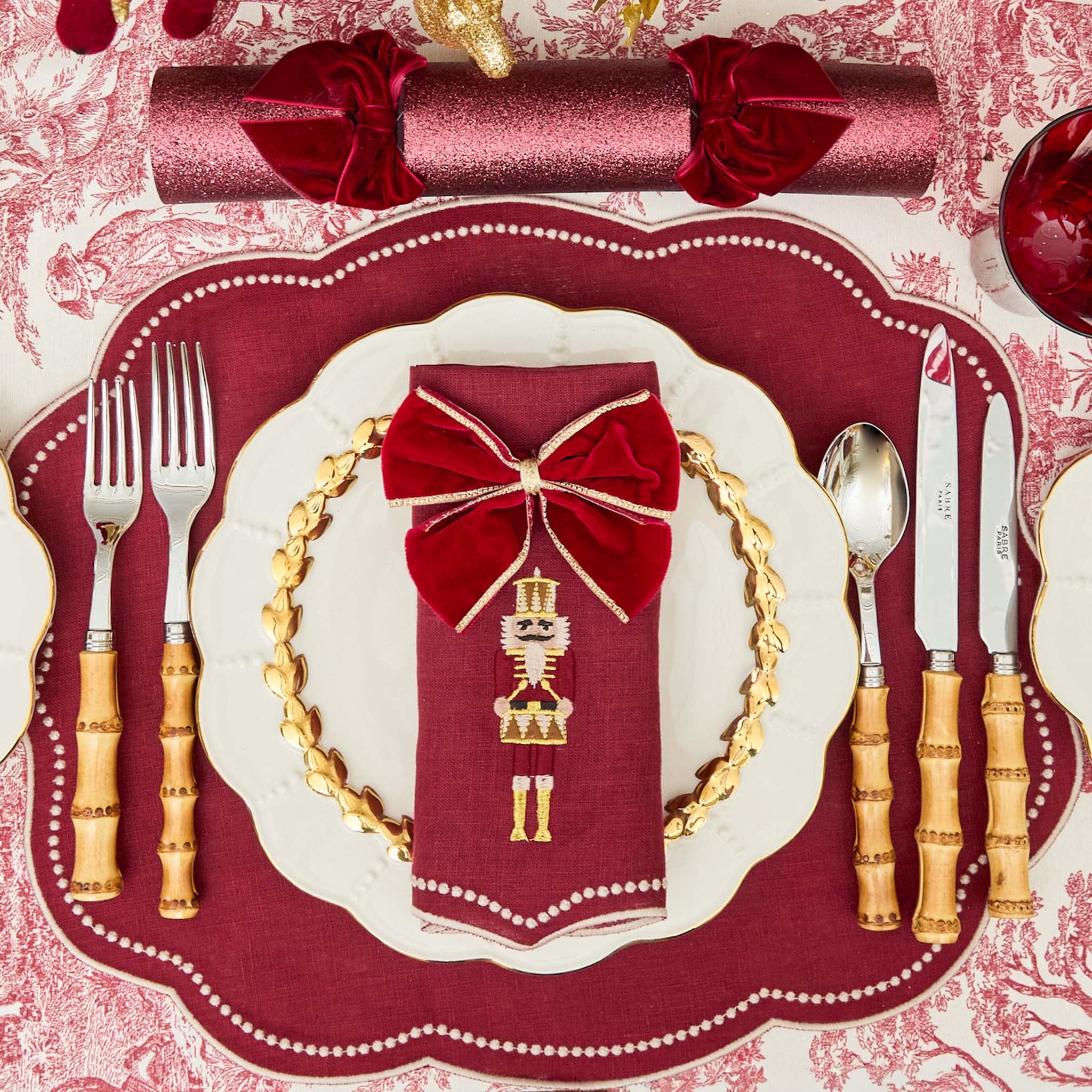 Decorative Christmas table setting with red napkin, gold cutlery, and festive background.