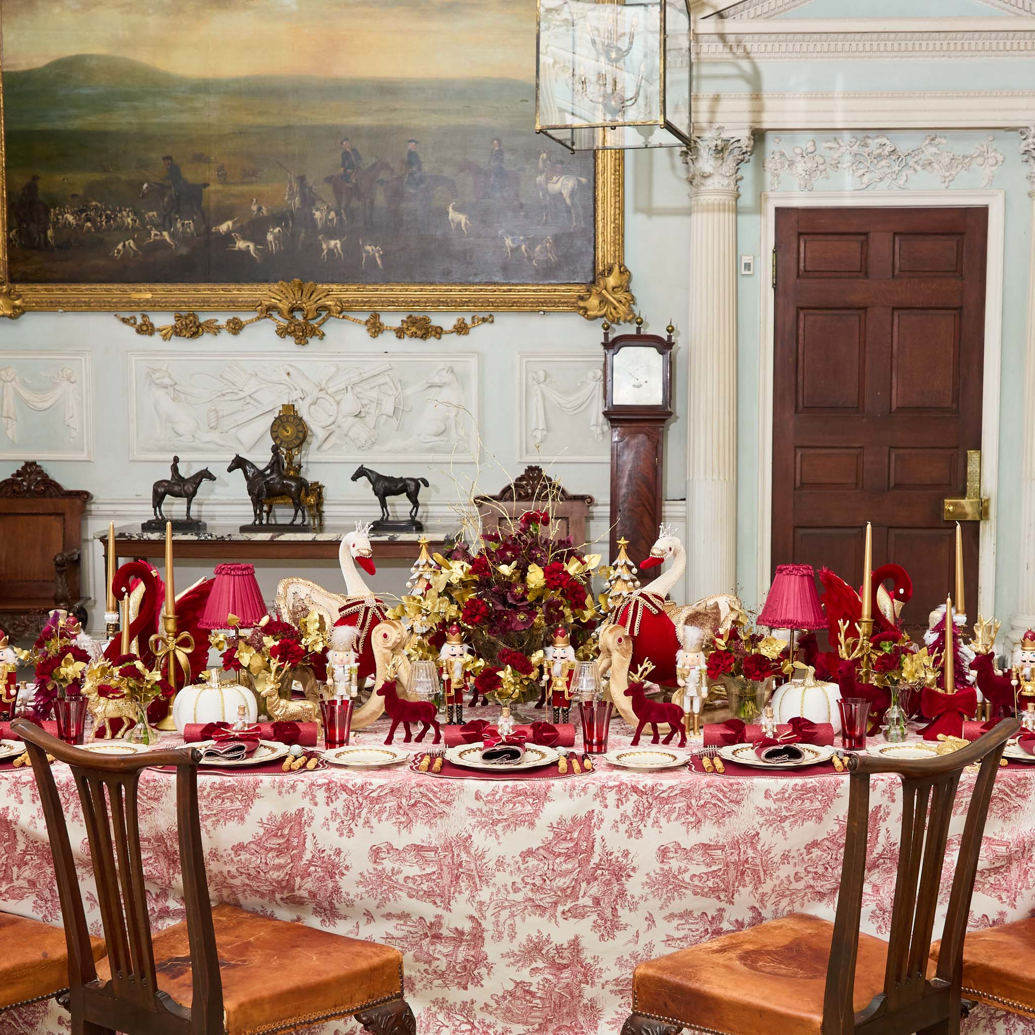 Decorative dining table set with red and gold tableware in a stately room.