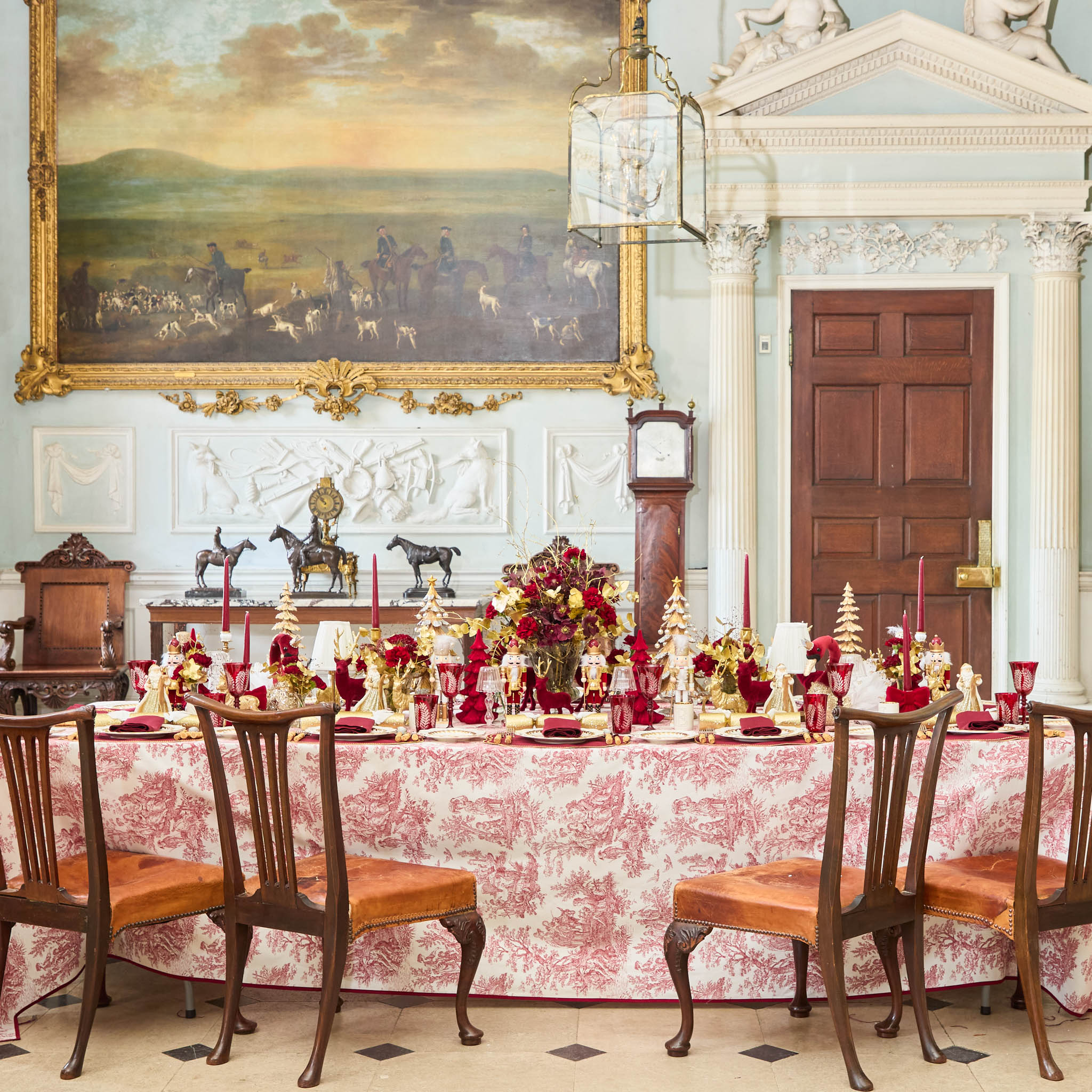 Decorative dining room with a long table set for a meal, ornate chairs, and a large painting on the wall.