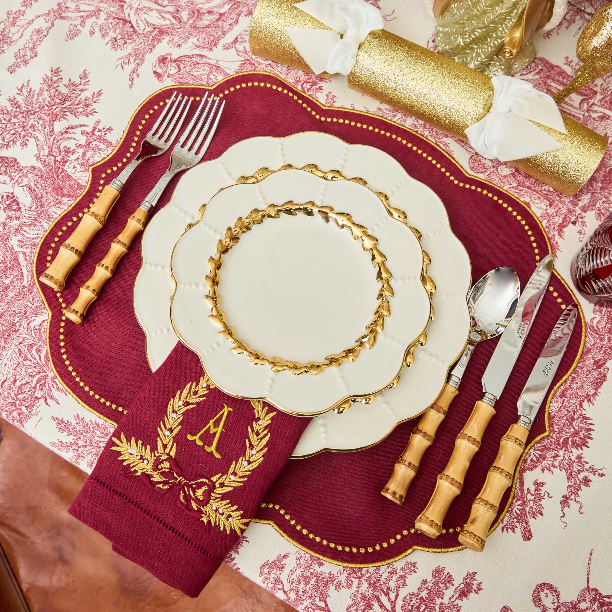 Decorative table setting with gold and red elements on a patterned tablecloth.