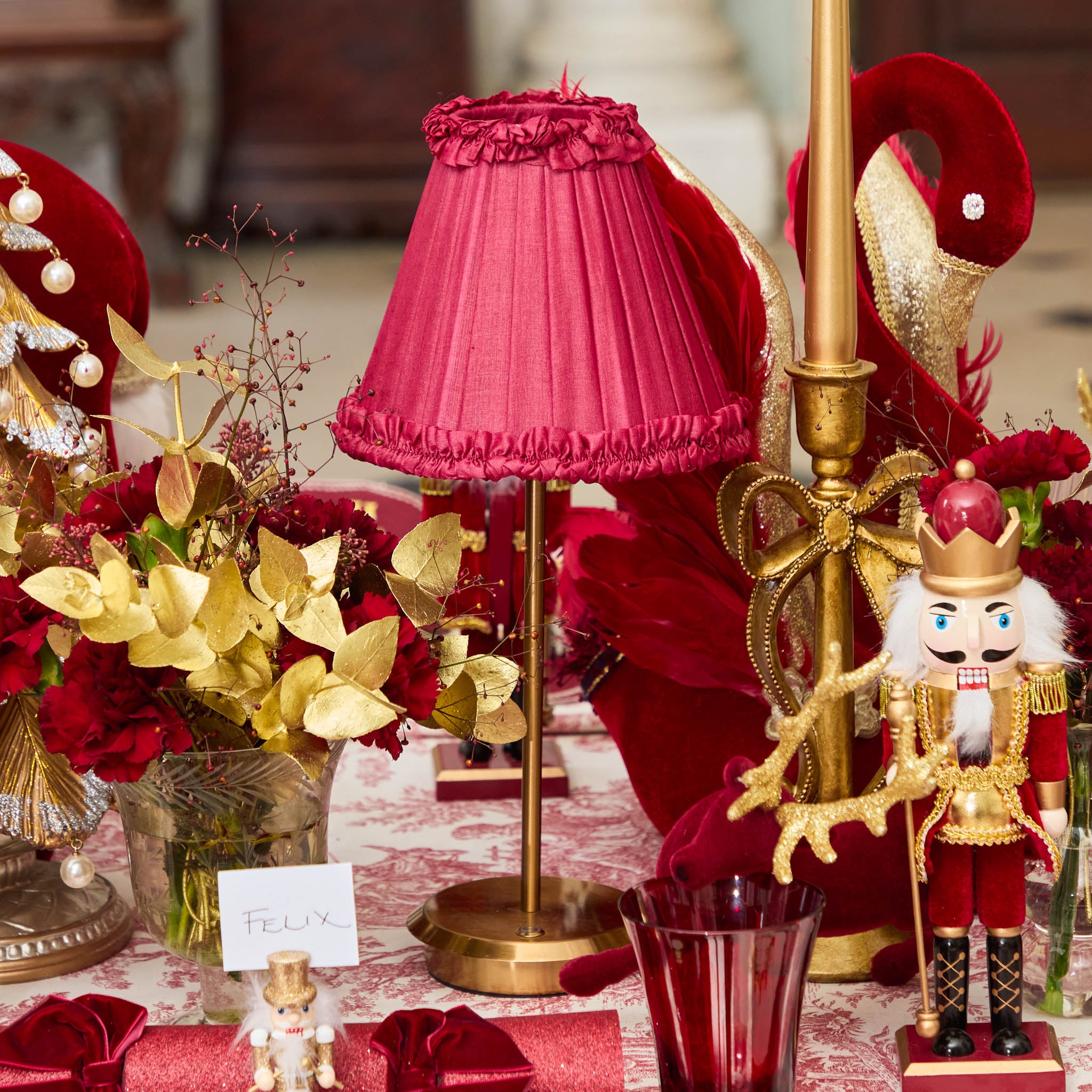 Decorative table setting with red and gold elements, including a pink lampshade and nutcracker figure.