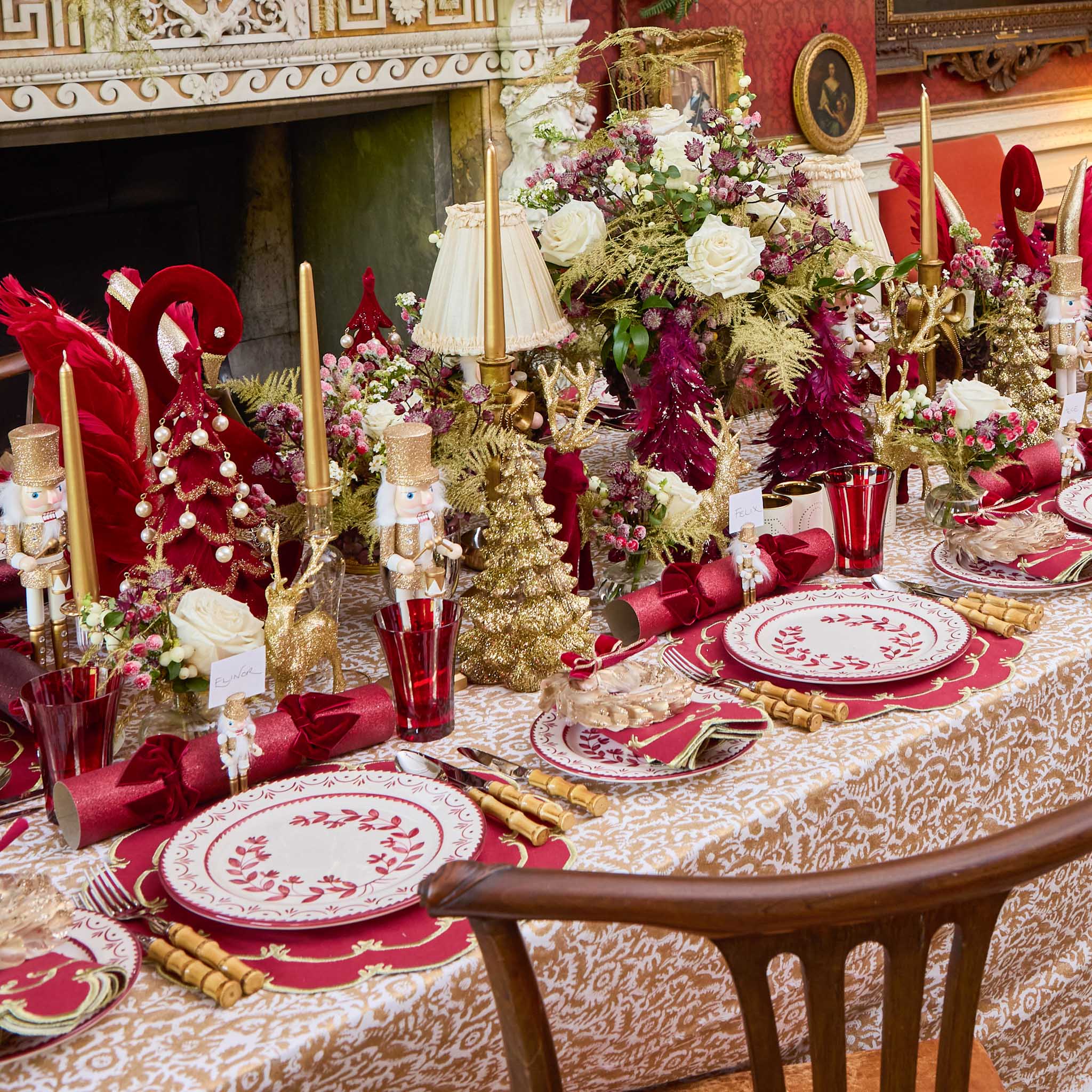 Decorative Christmas table setting with red and gold accents, floral arrangements, and festive tableware.
