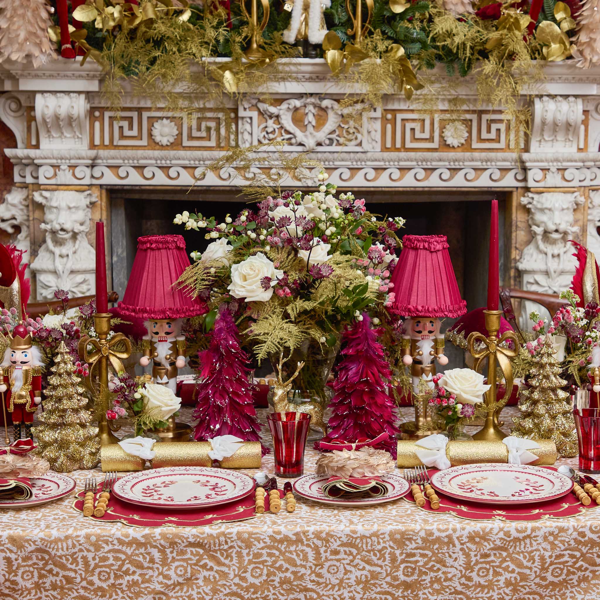 Decorative Christmas table setting with red and gold elements in front of a fireplace.