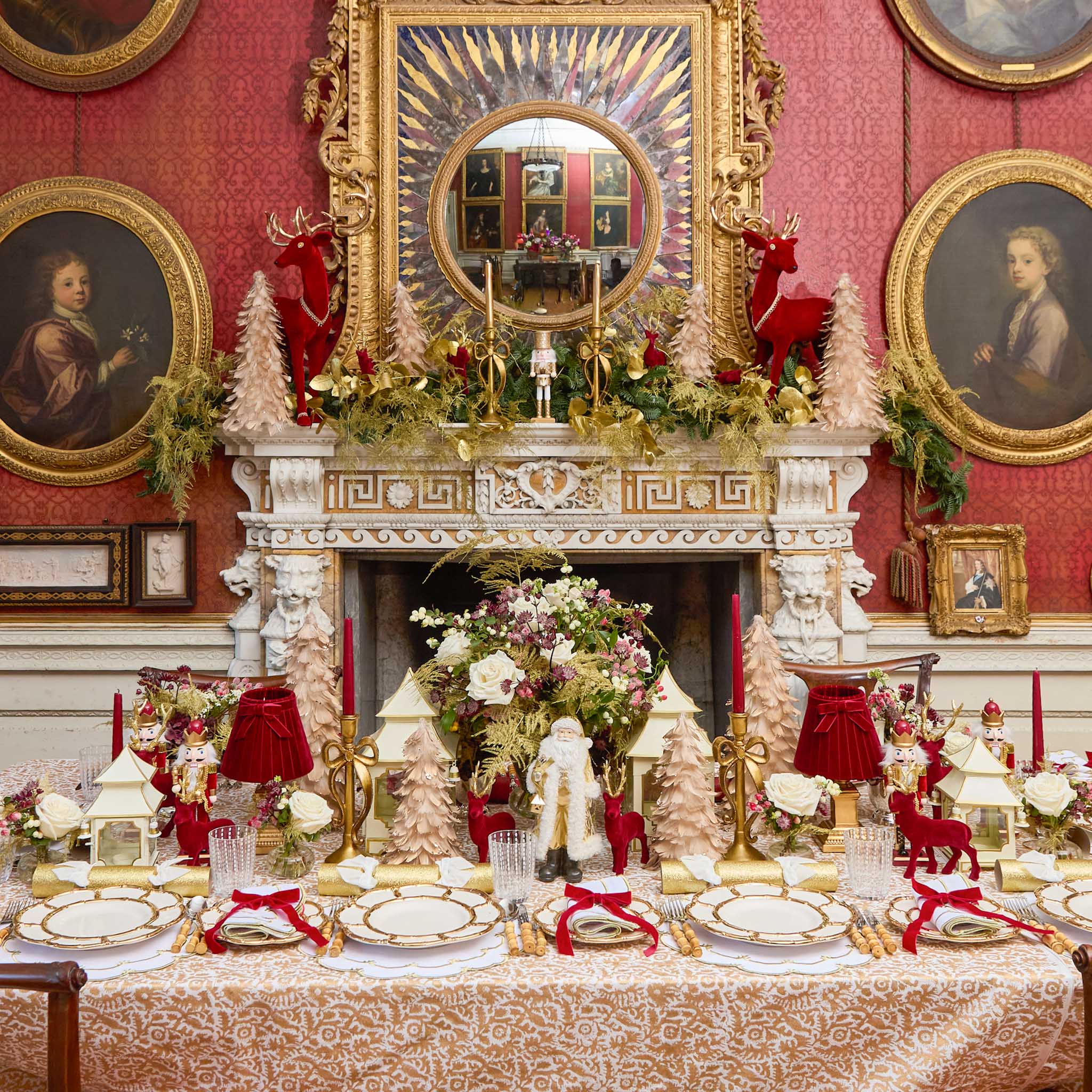Decorative Christmas table setting in a room with red walls, gold accents, and classical paintings.