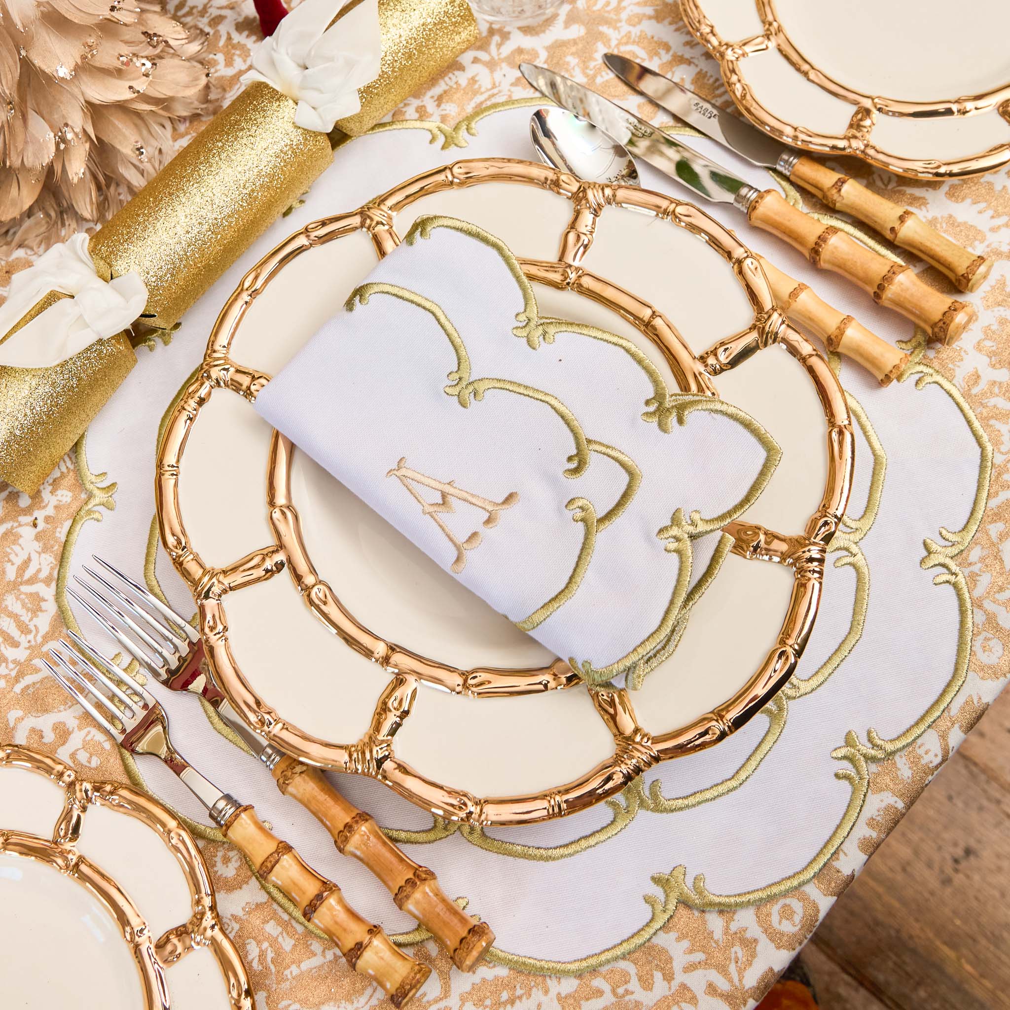Decorative table setting with gold charger plate, napkin, and cutlery on a patterned tablecloth.