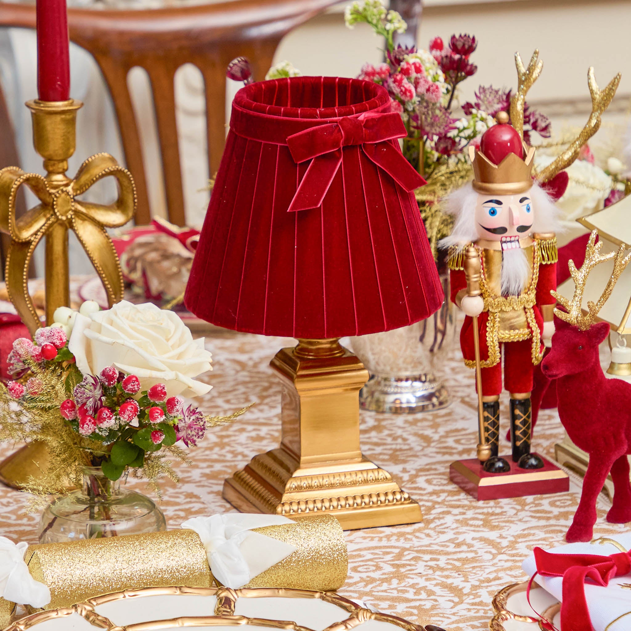 Decorative table setting with red lamp, nutcracker, and reindeer on a patterned tablecloth.