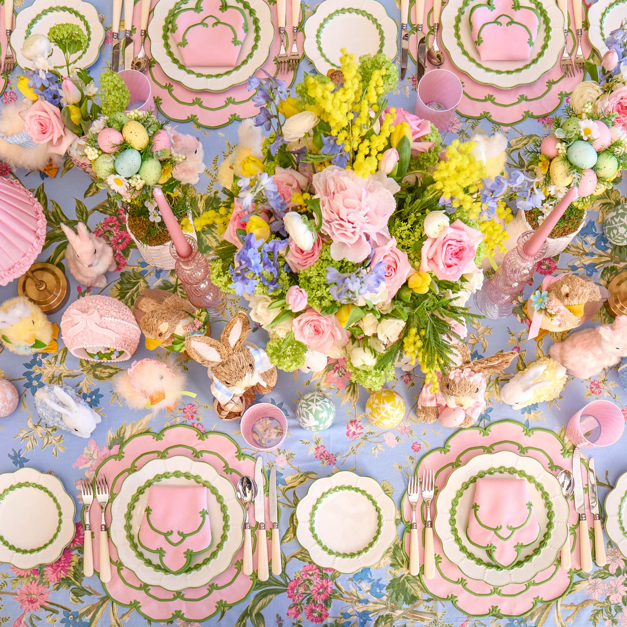 Colorful Easter-themed table setting with floral arrangements, bunny figurines, and pastel plates.