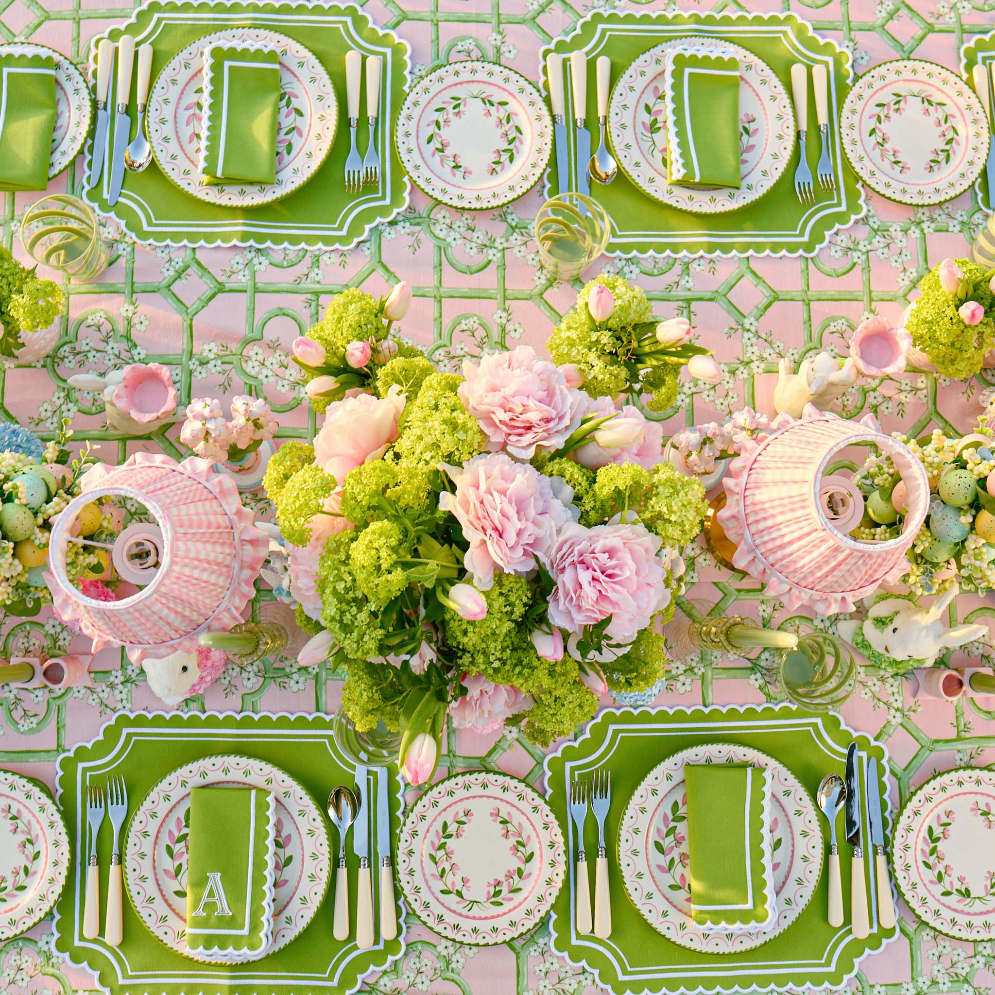 Decorative table setting with green and pink plates, flowers, and cutlery on a patterned tablecloth.
