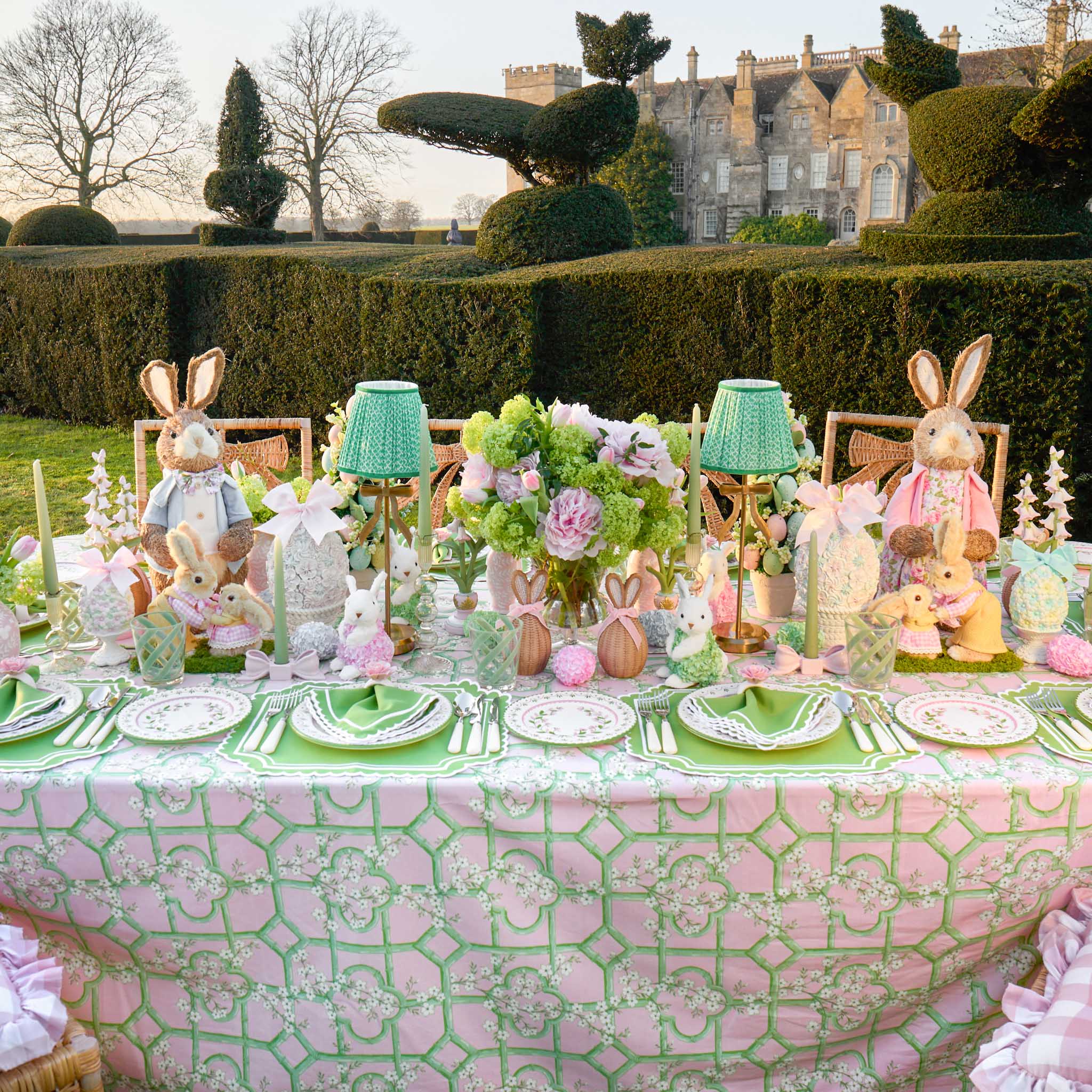 Easter-themed table setting with decorative rabbits, flowers, and pastel colors in a garden setting.