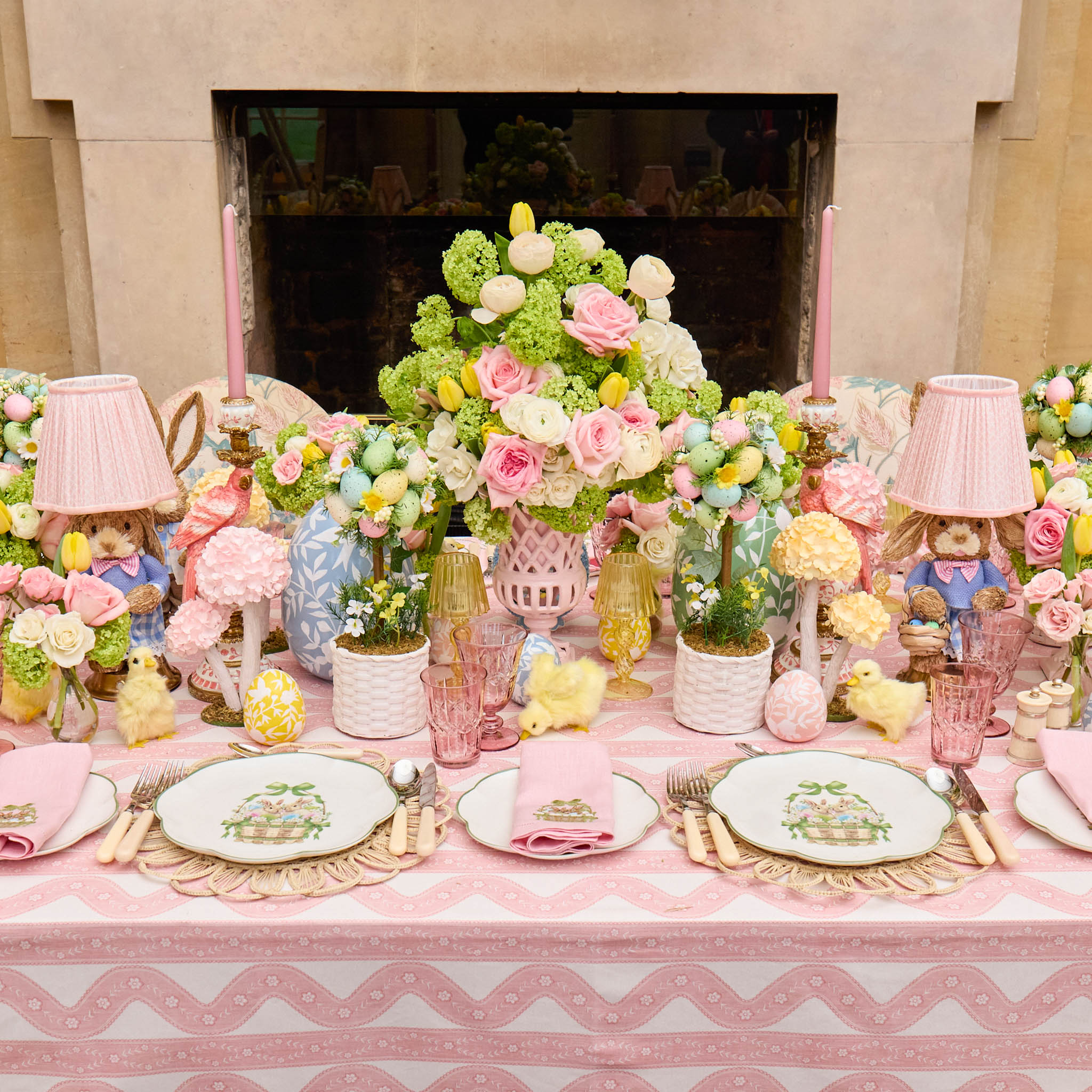 Decorative table setting with flowers, lamps, and tableware in a room with a fireplace.