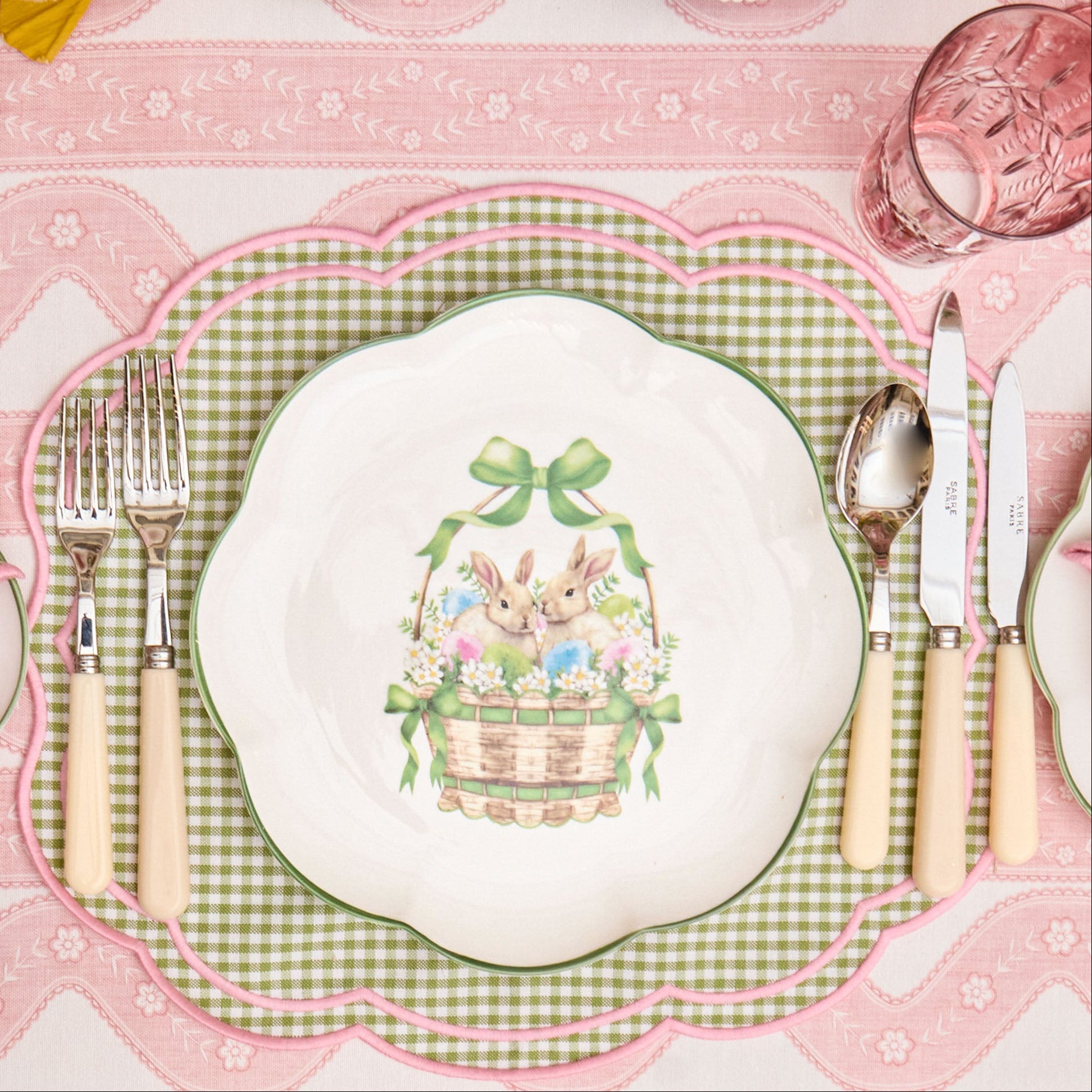Easter-themed place setting with bunny design on a pink and white checkered tablecloth.