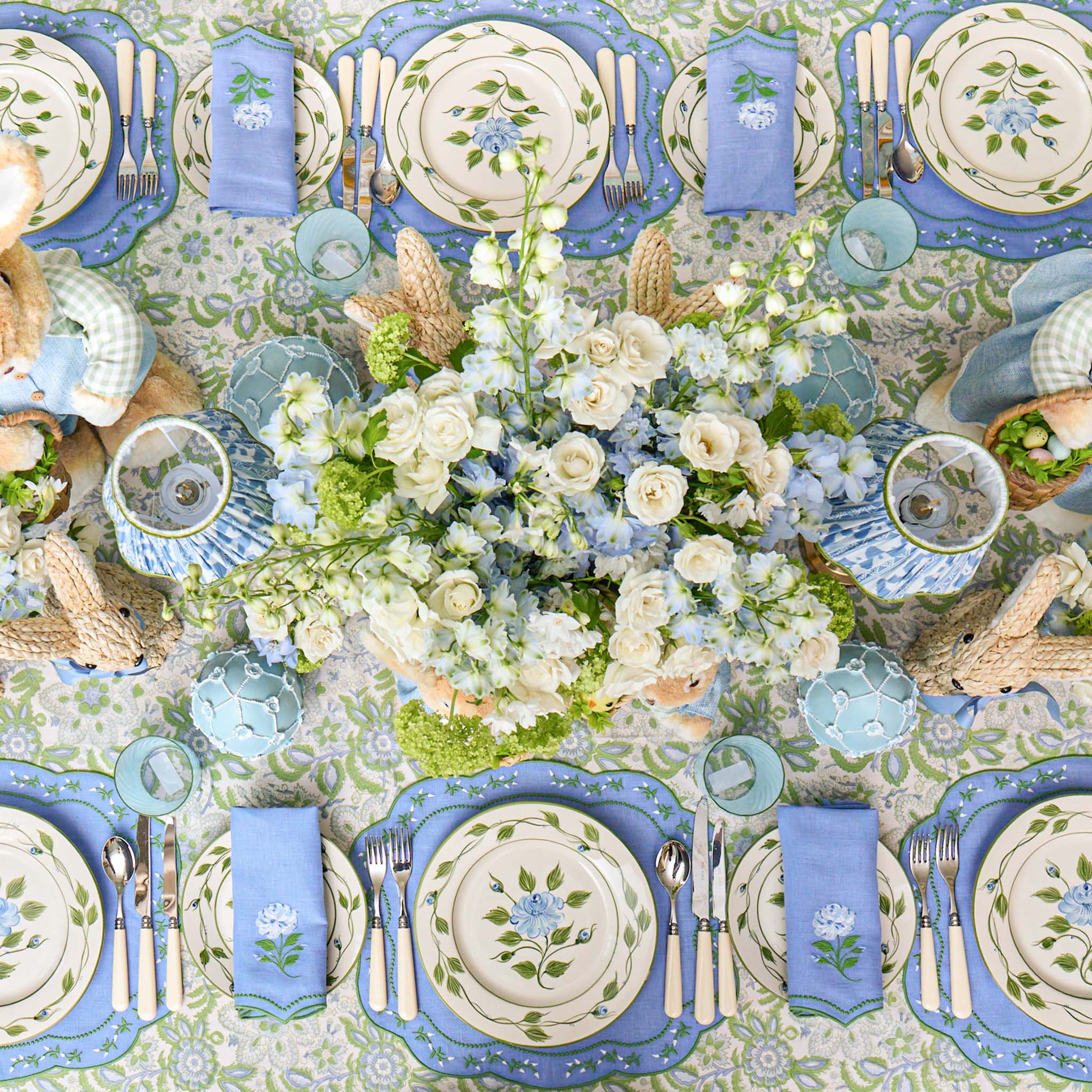 Elegant table setting with blue and green plates, silverware, and floral centerpieces.