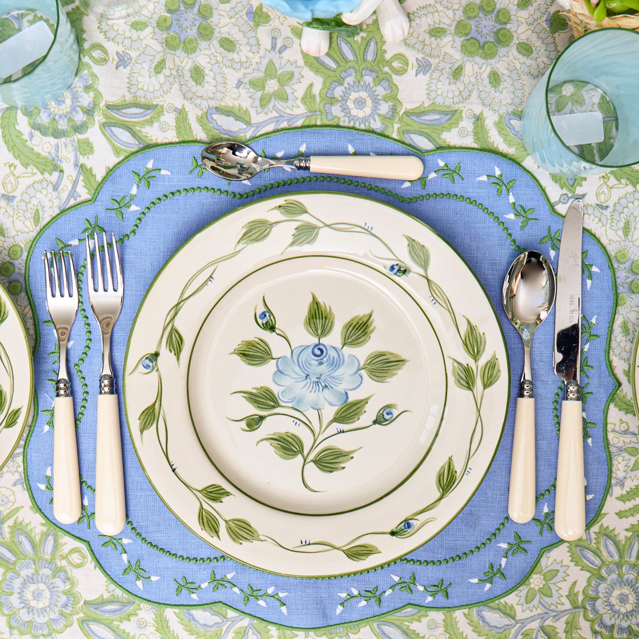 Decorative table setting with floral plates and cutlery on a patterned tablecloth.