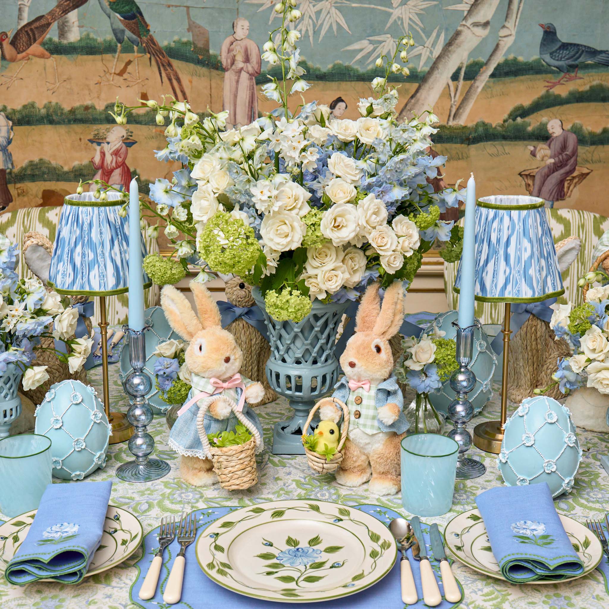 Easter table setting with bunny figurines, floral arrangements, and decorative eggs.