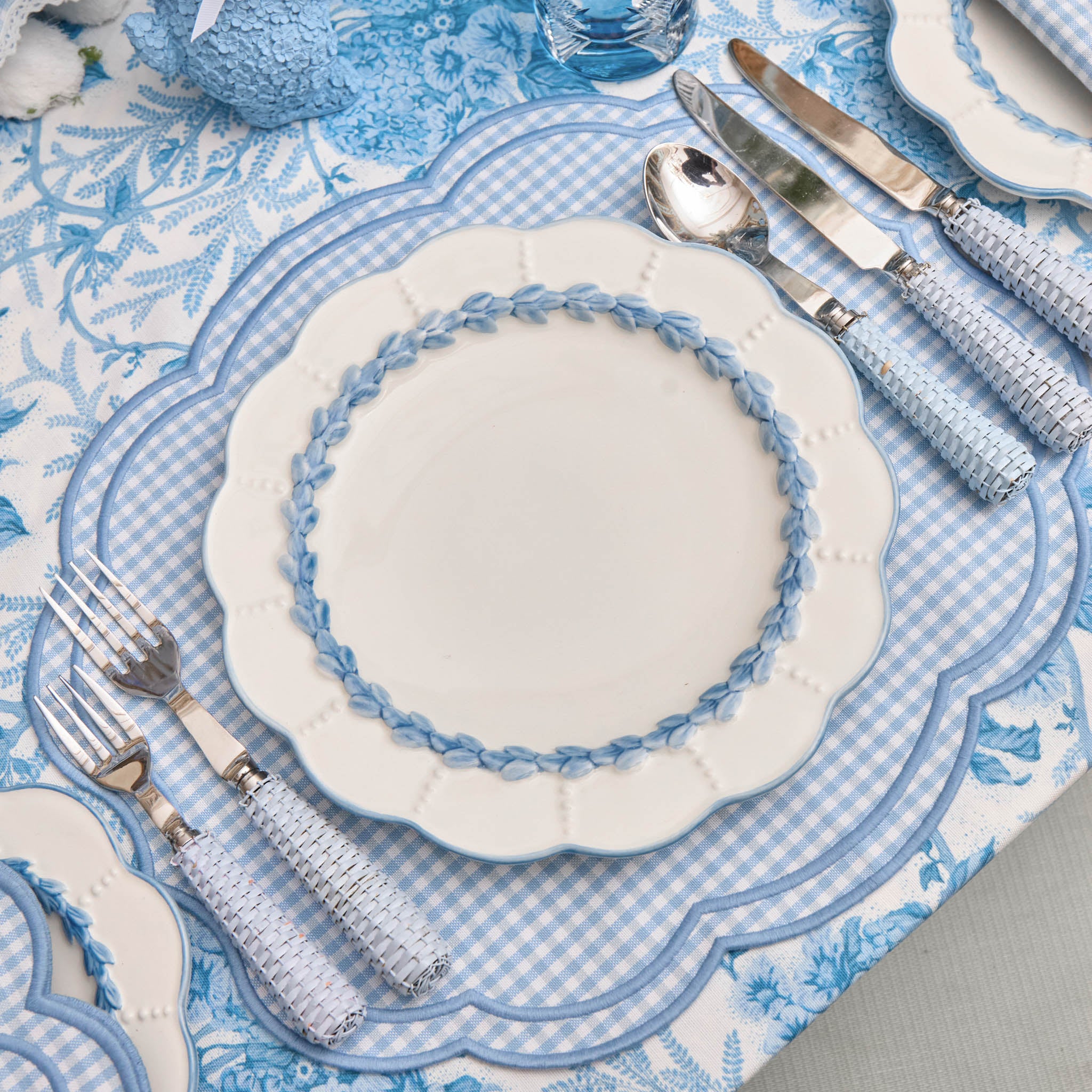 Blue and white table setting with decorative plates and cutlery on a checkered tablecloth.