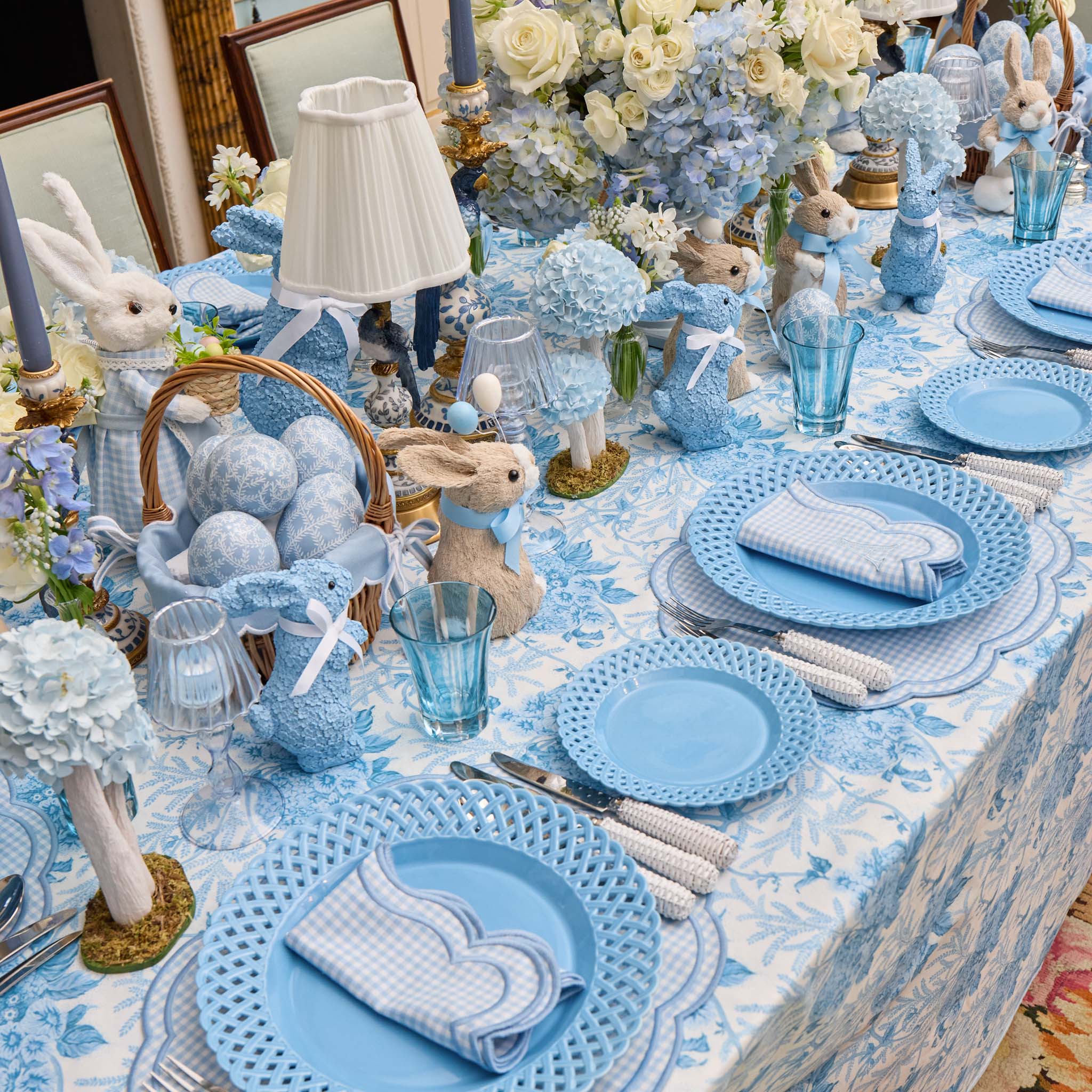 Easter-themed table setting with blue and white decorations, including bunny figurines and floral arrangements.