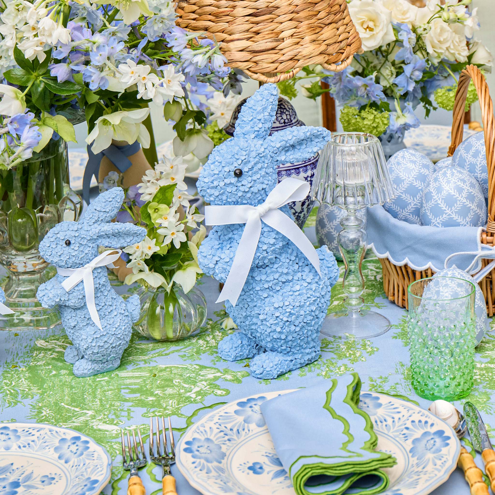 Decorative Easter table setting with blue bunny figurines, floral arrangements, and Easter-themed tableware.