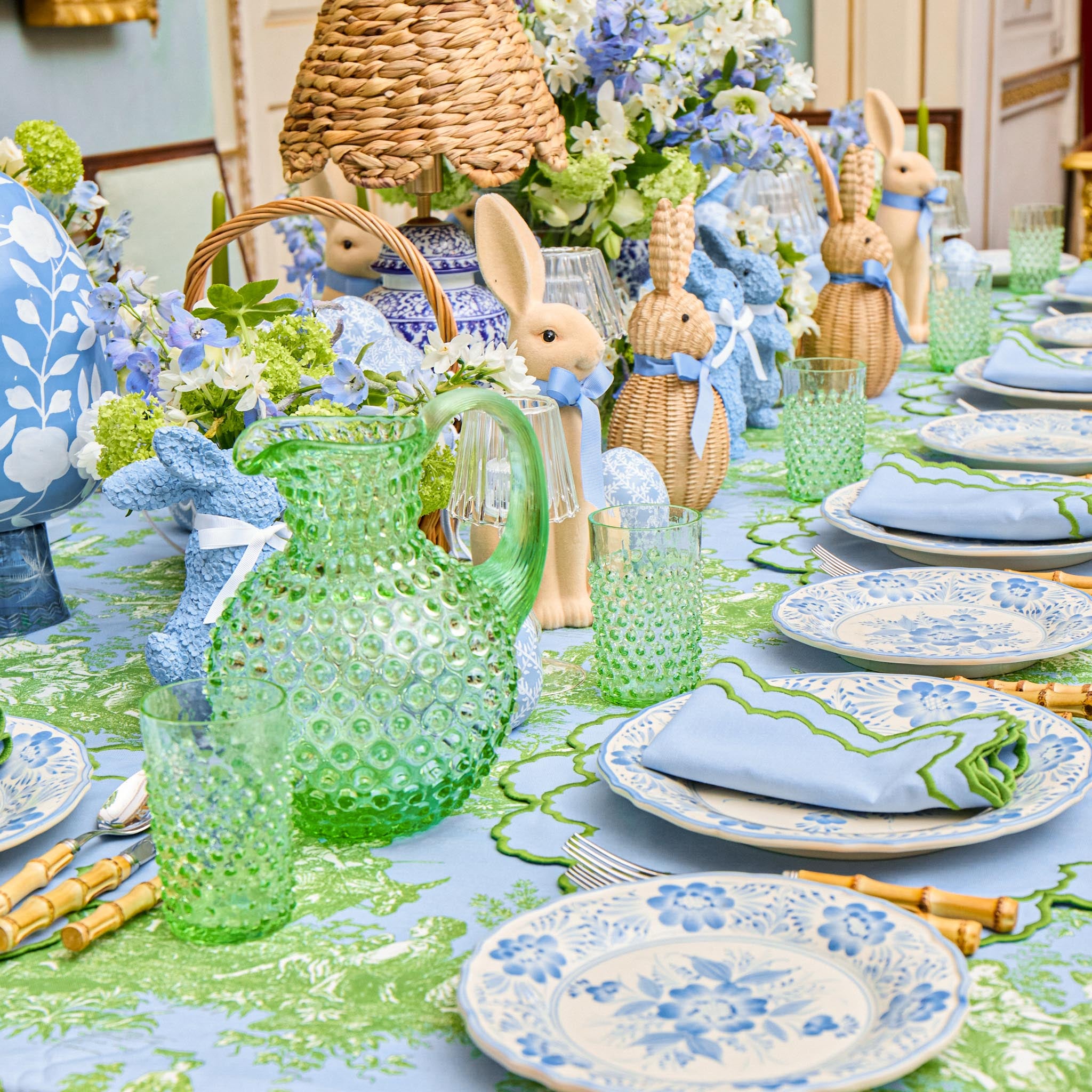 Easter-themed table setting with green glass pitcher, bunny decorations, and floral arrangements.