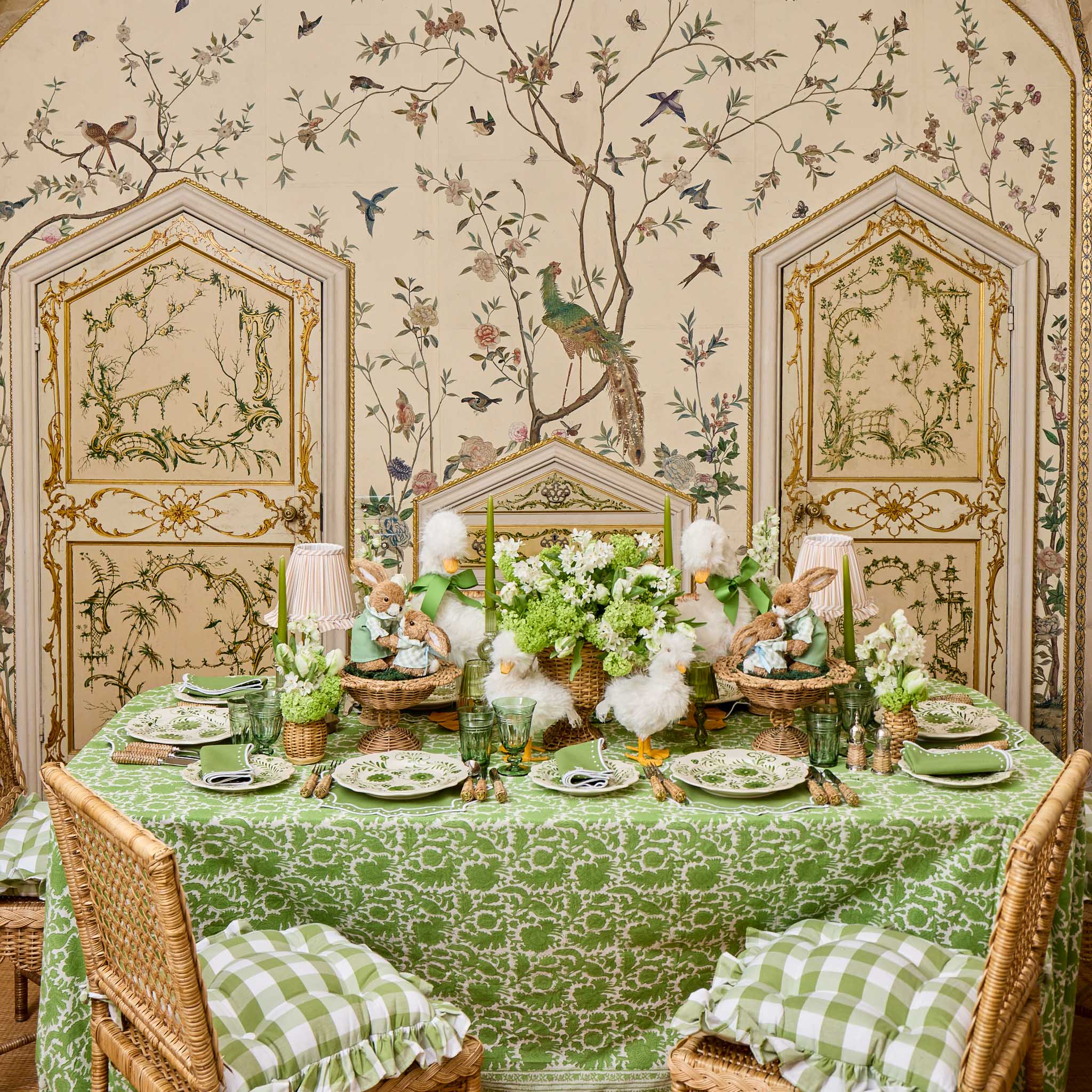 Decorative table setting with green tablecloth and floral arrangements in a room with ornate wallpaper.