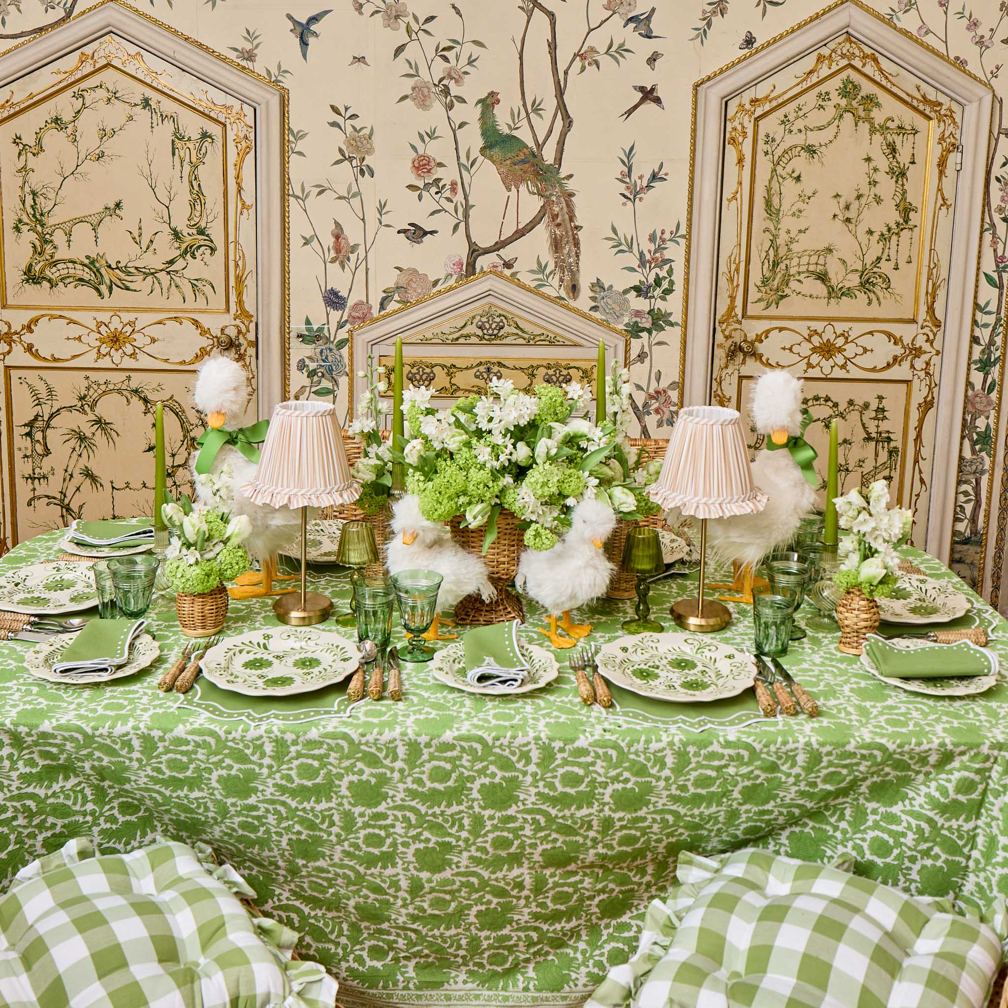 Decorative table setting with green tablecloth and floral arrangements in a room with ornate walls.