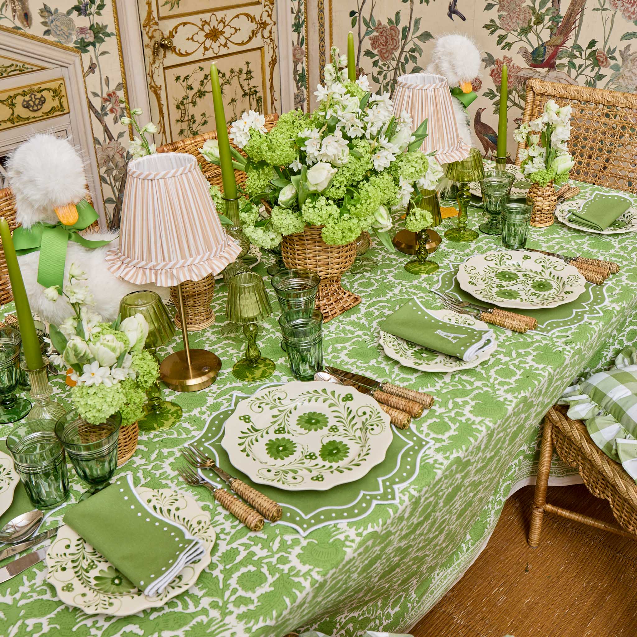 Decorative table setting with green and white theme, including tablecloth, plates, glasses, and centerpieces.