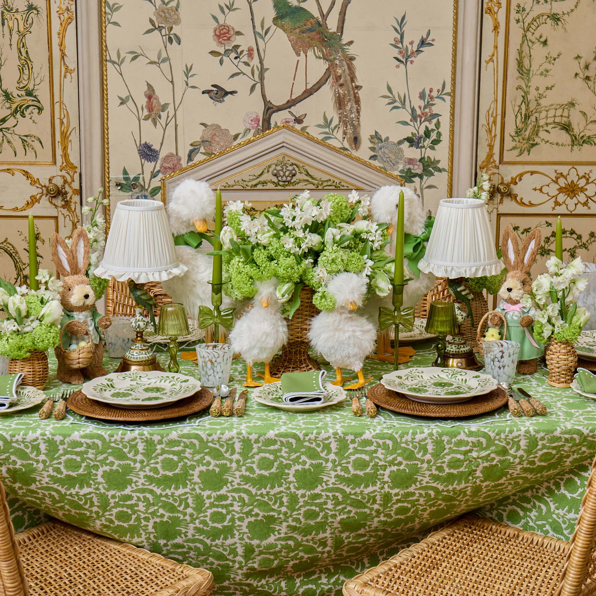 Easter-themed table setting with green tablecloth, bunny decorations, and floral arrangements.