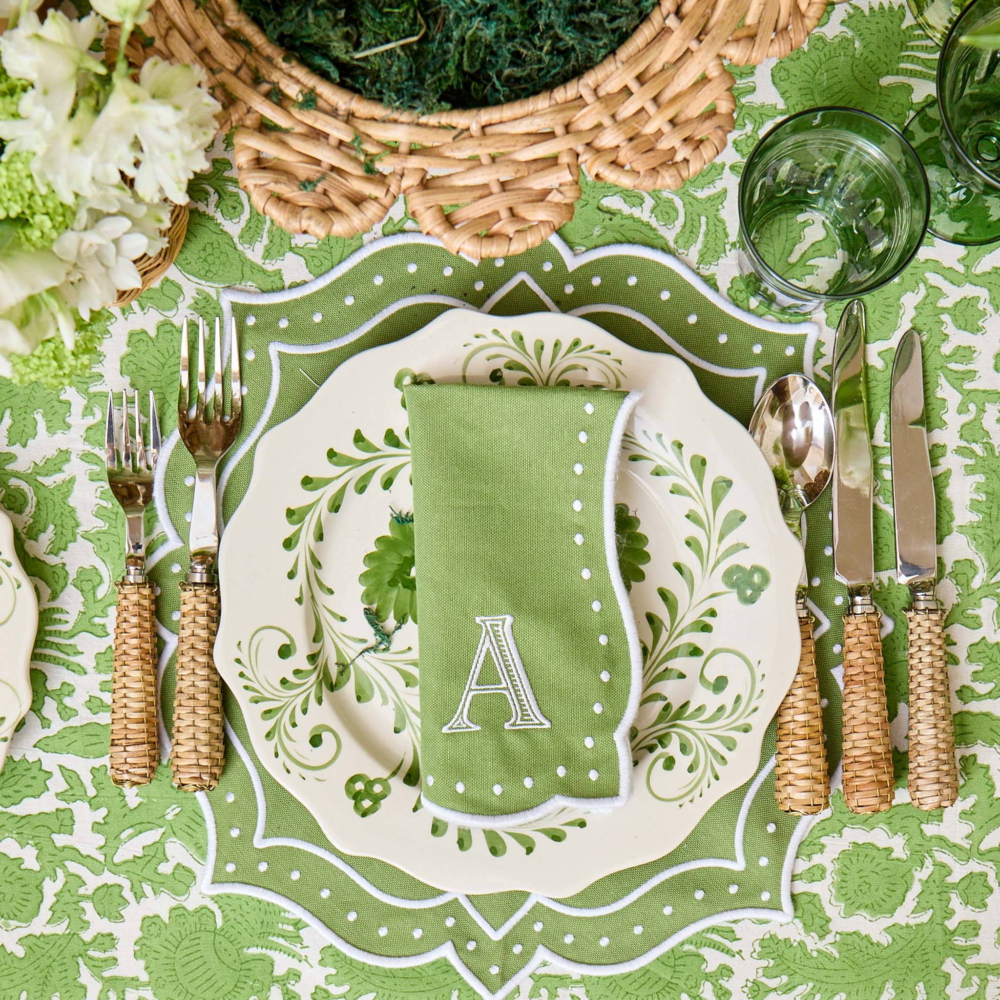 Green and white place setting with monogrammed napkin on a patterned tablecloth.