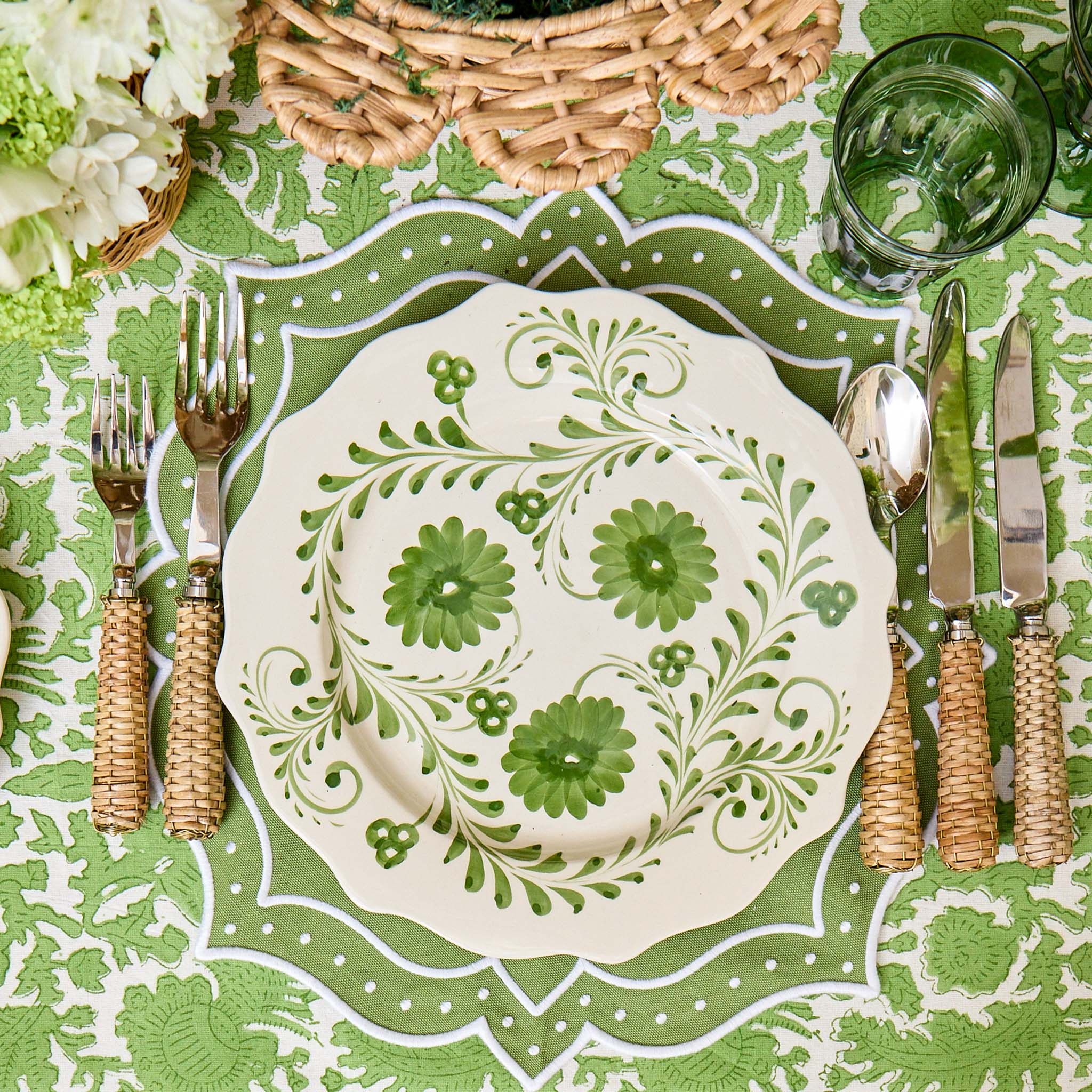 Decorative table setting with a floral-patterned plate, cutlery, and green tablecloth.