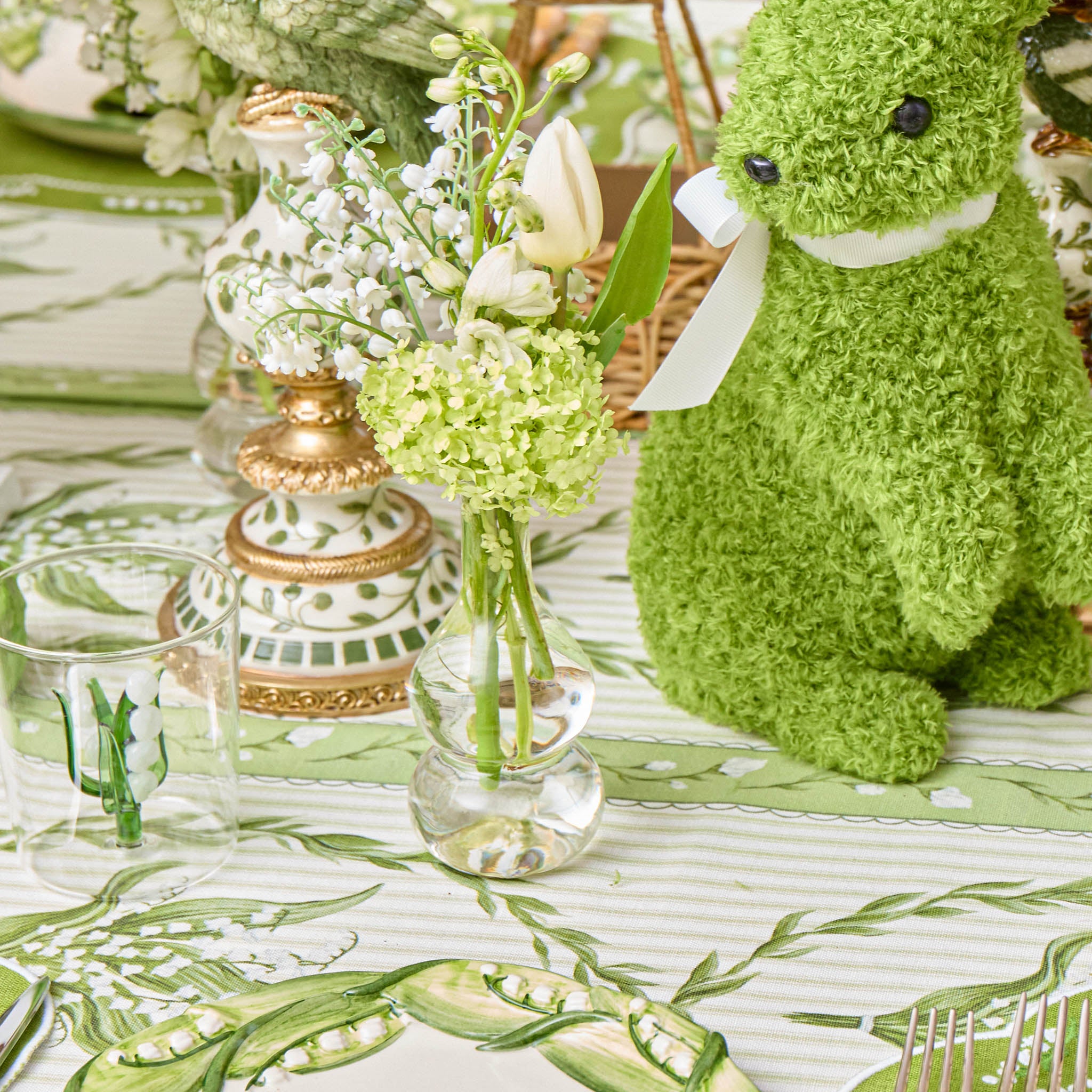 Green plush toy next to floral arrangement on a decorative tablecloth
