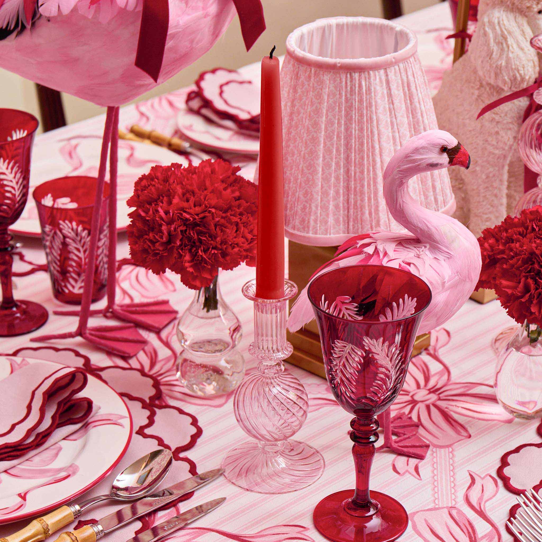 Decorative table setting with pink flamingo, red glasses, and floral arrangements on a patterned tablecloth.
