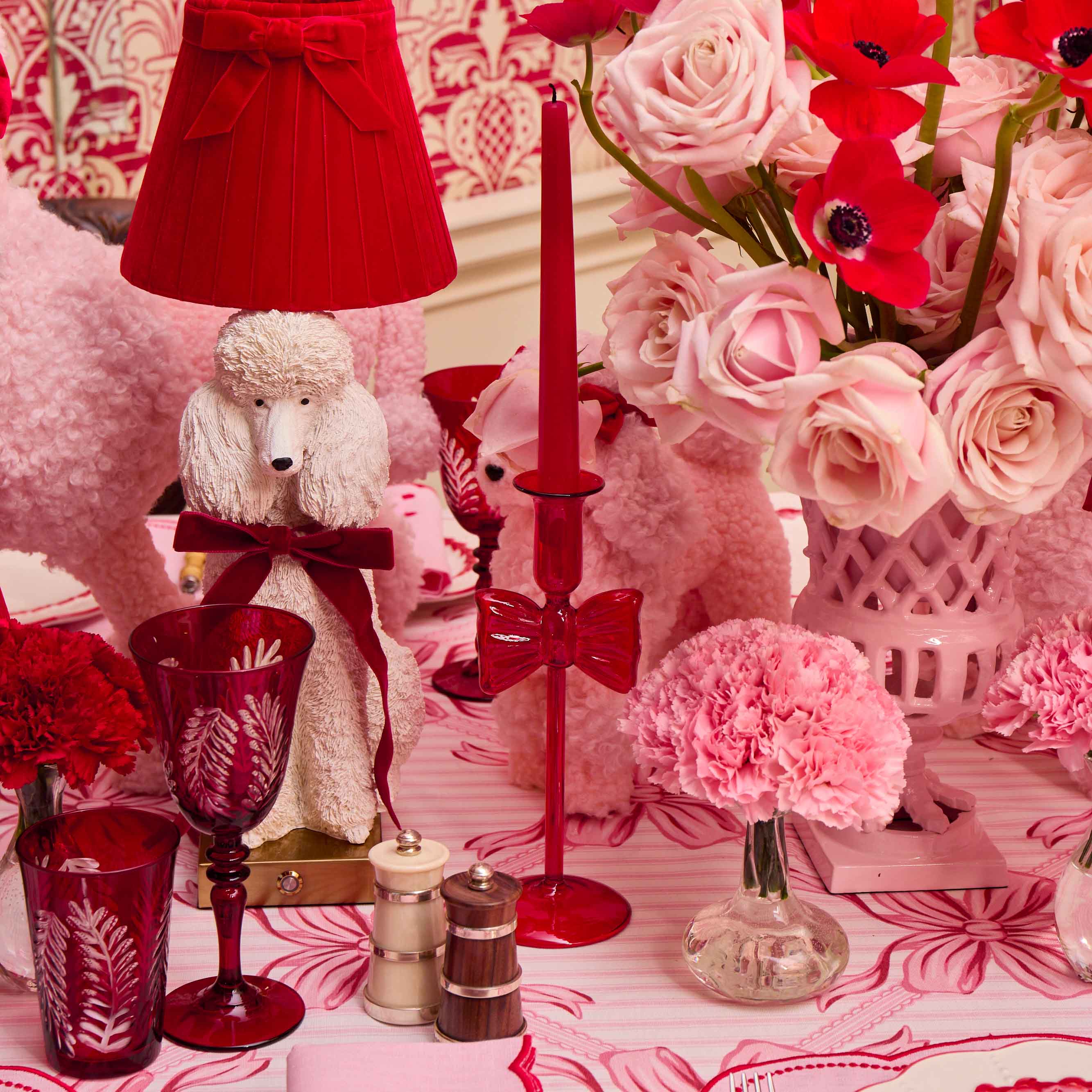 Decorative table setting with red and pink elements including a lamp, flowers, and candles.