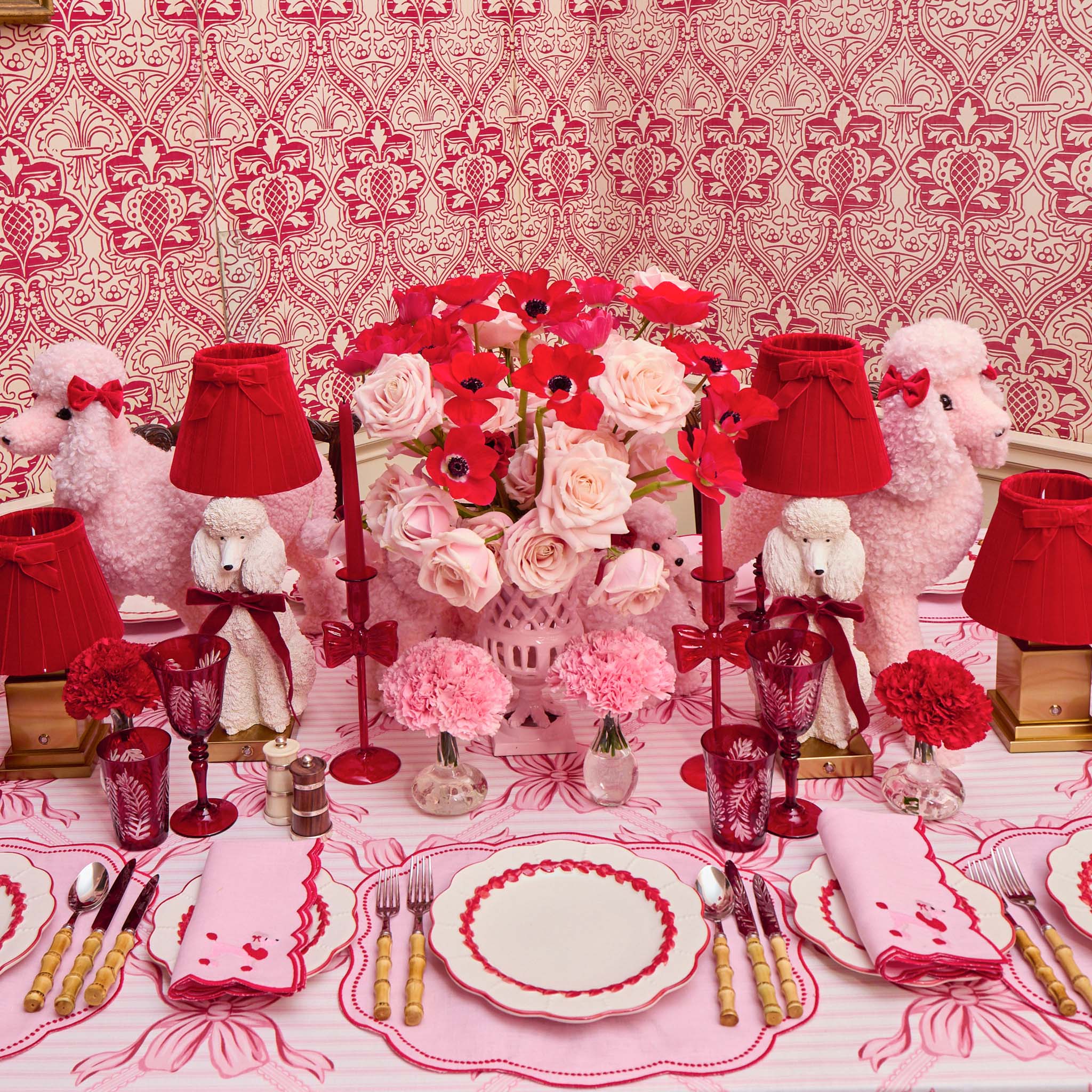 Decorative table setting with pink and red theme, including flowers, lamps, and poodles.