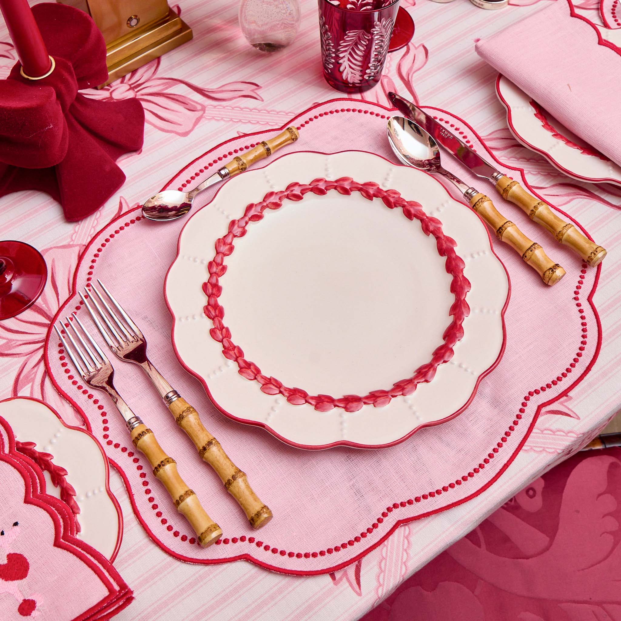 Decorative table setting with pink and white plates, cutlery, and a red bow.