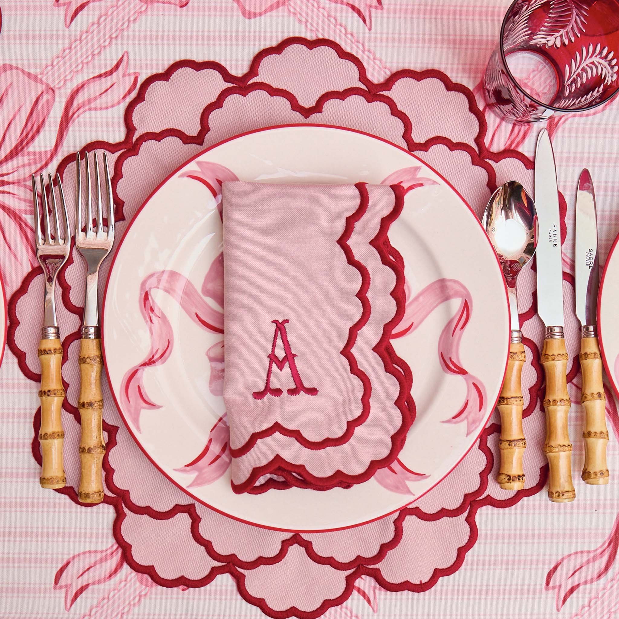 Dining table setting with pink and white plates, napkin, and cutlery on a matching pink tablecloth.