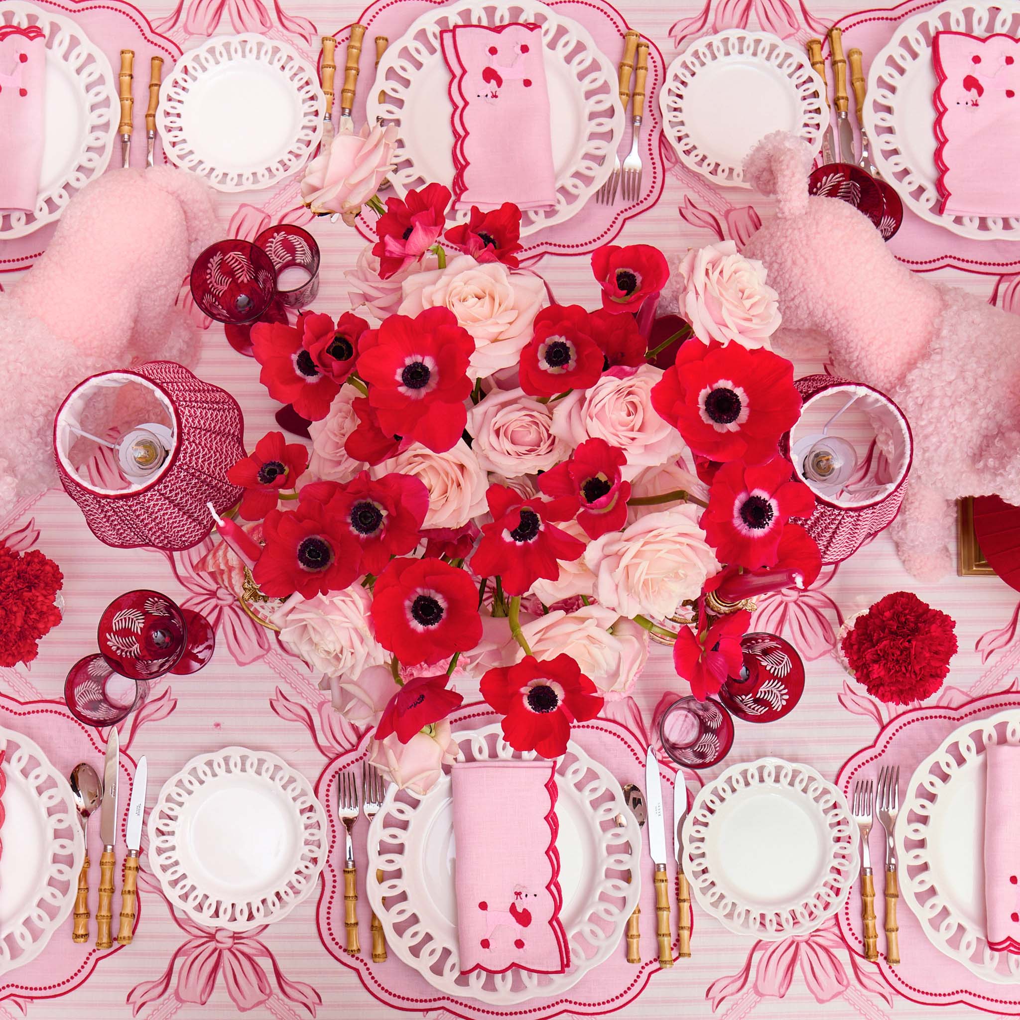 Decorative table setting with red and white flowers on a pink tablecloth.