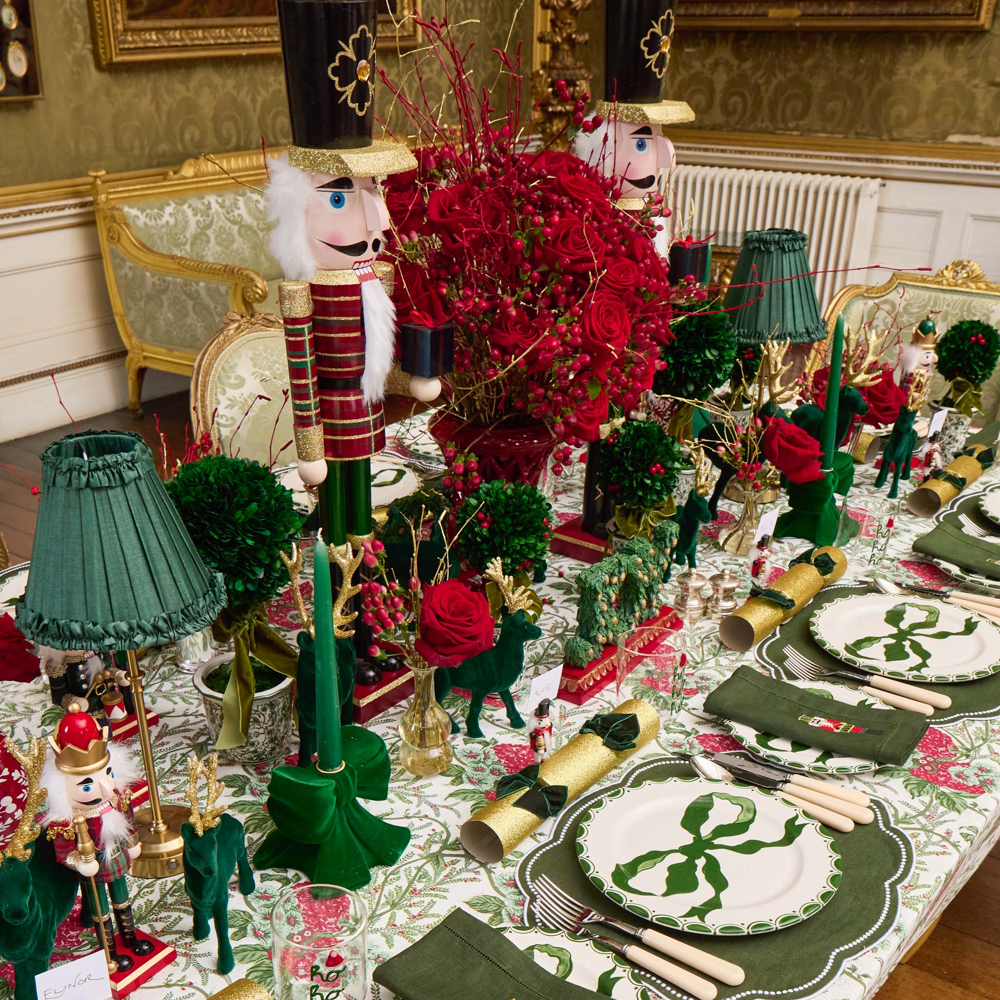 Decorative table setting with nutcrackers, red flowers, and green tableware in a festive room.